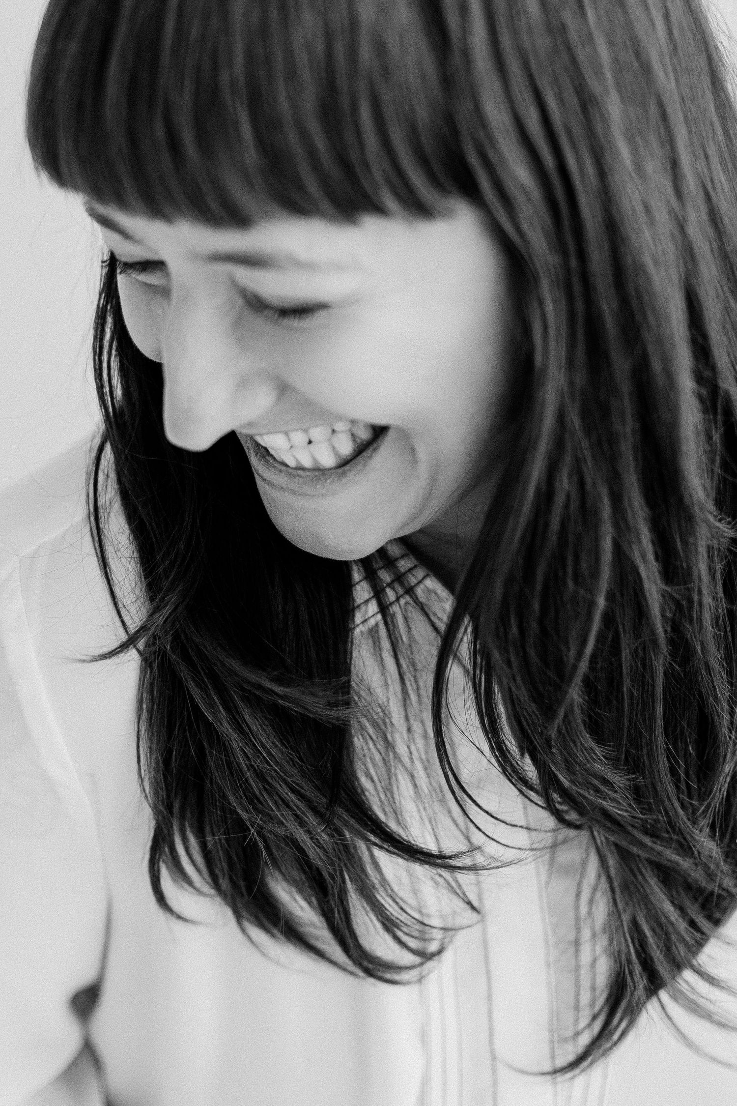 Black and white close-up portrait of a smiling woman with bangs and long dark hair looking down.