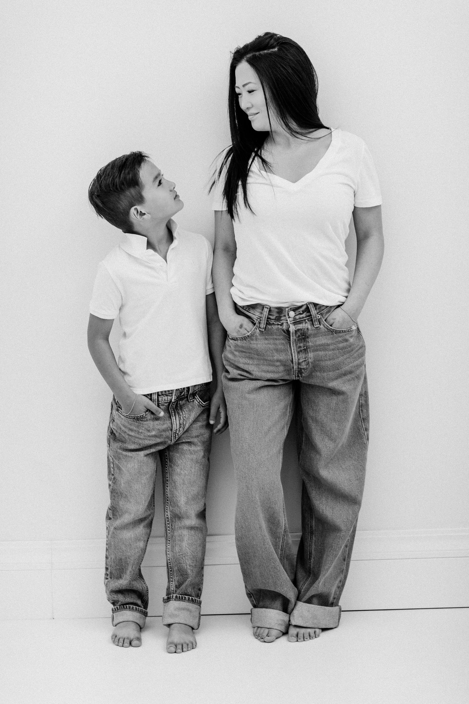 A black and white photo of a boy and his dark-haired mother in matching white tees and jeans.