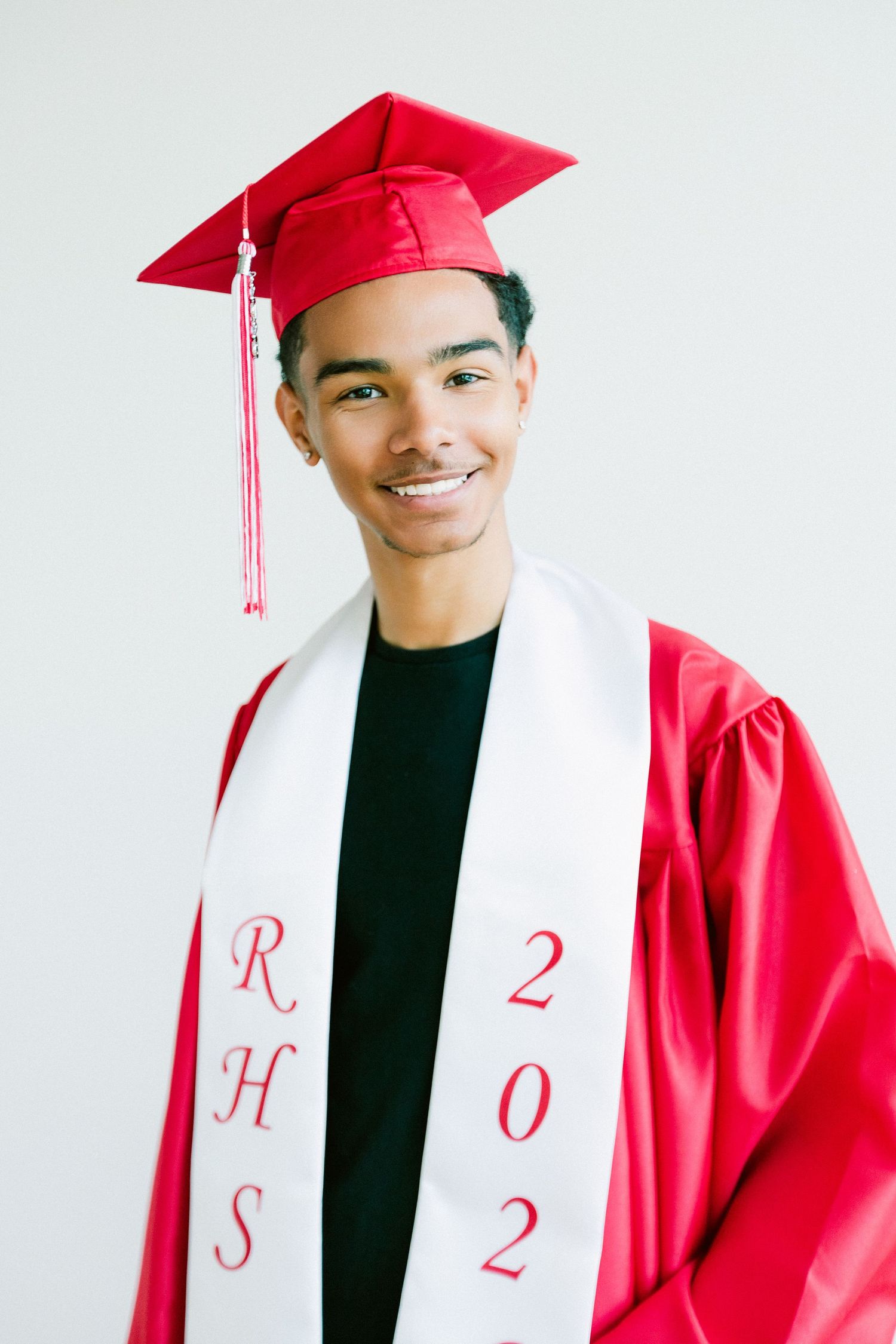 Smiling young man in red graduation cap and gown with RHS 2022 stole against white background.