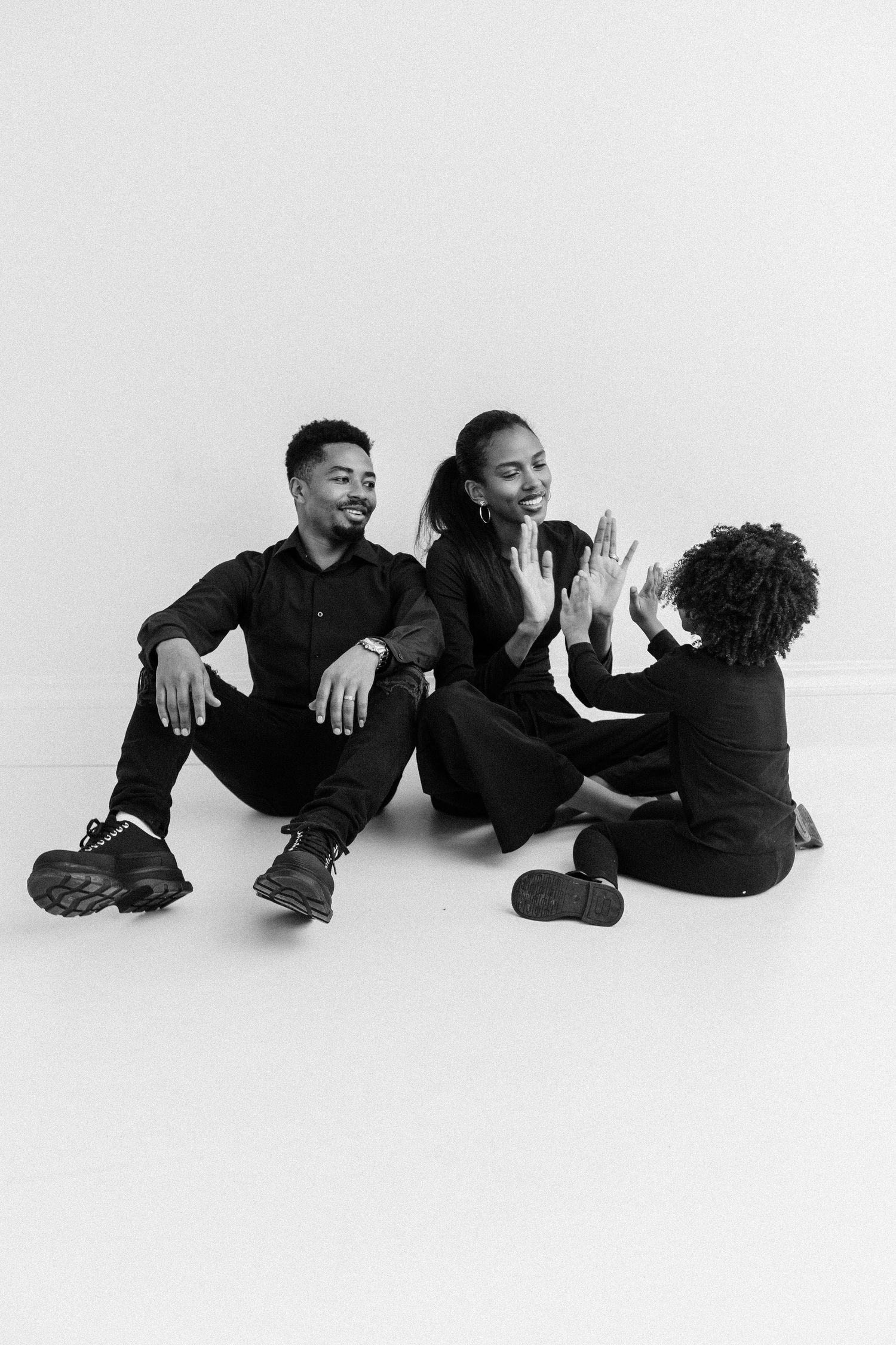 Black and white photo of a family sitting on floor, two adults smiling while child gives high five.