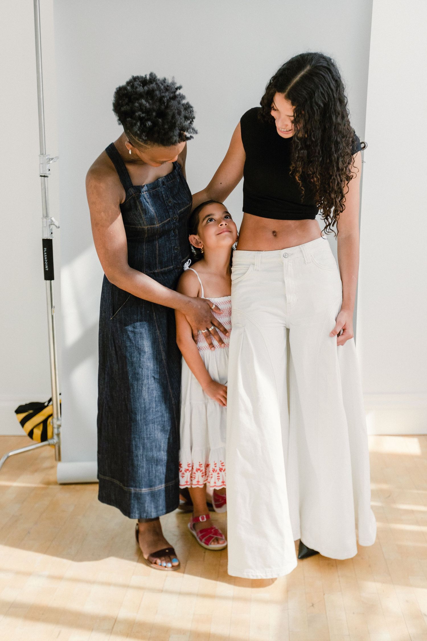 Two women and a young girl share a tender moment together in a bright studio setting.