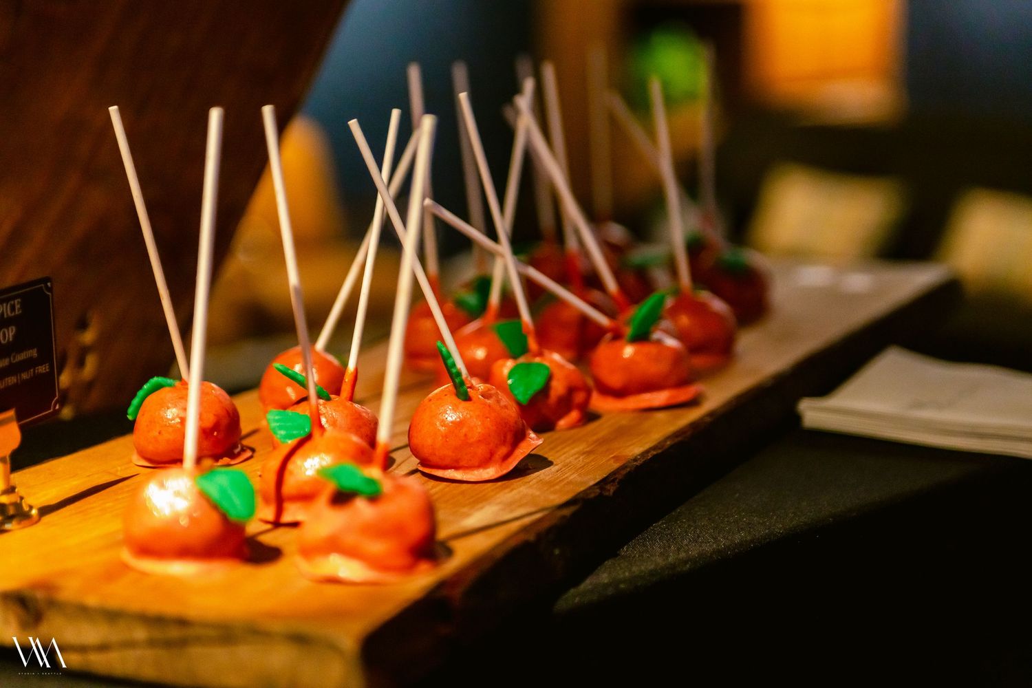 Decorative caramel apple cake pops displayed on a rustic wooden board at an elegant event.