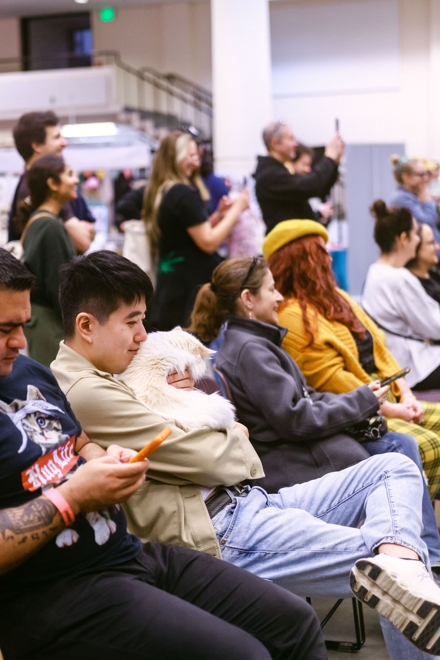 Diverse crowd seated at an indoor event, with a young man holding a small pet in his lap.