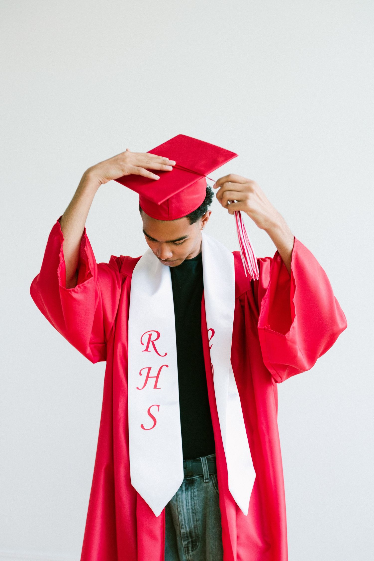Student in red graduation cap and gown with RHS stole adjusting mortarboard tassel before ceremony.