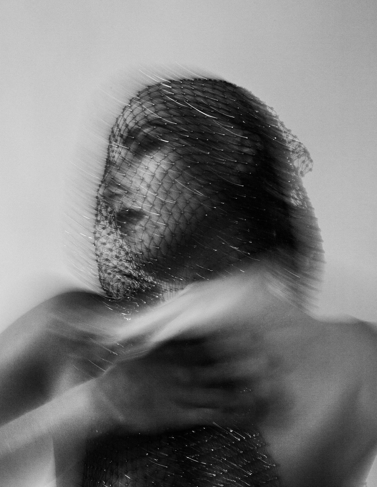 Black and white blurred portrait of a person with a net veil over their face, creating an ethereal, mysterious effect.