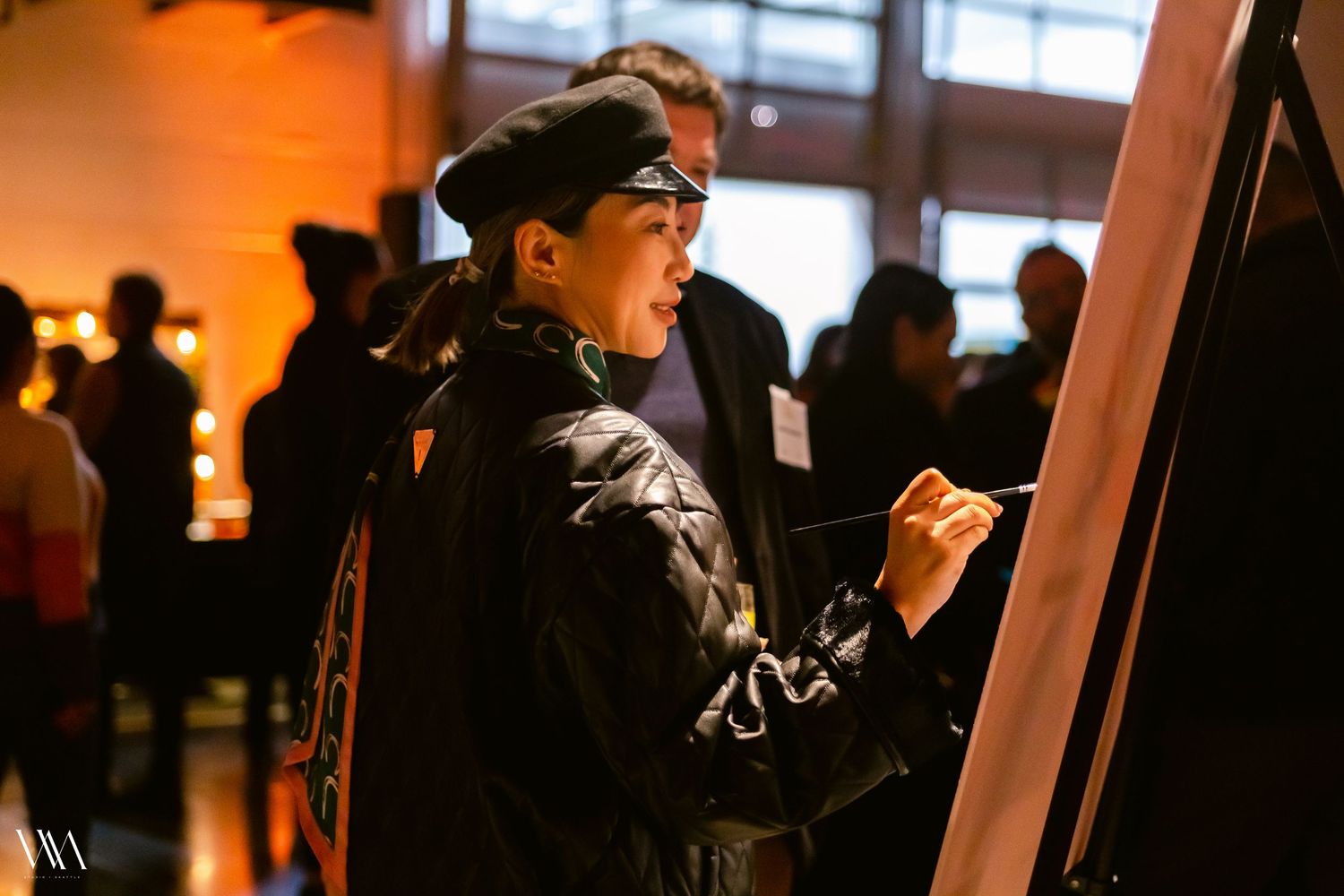A young artist wearing a beret sketches on a canvas at an indoor art event.