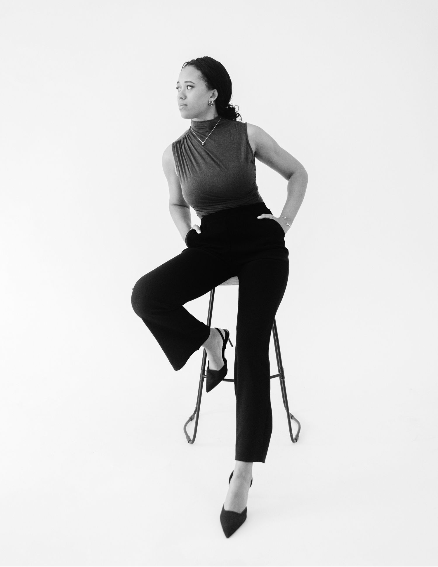Woman posing on a stool in black wide-leg pants and heels in a black and white photo.