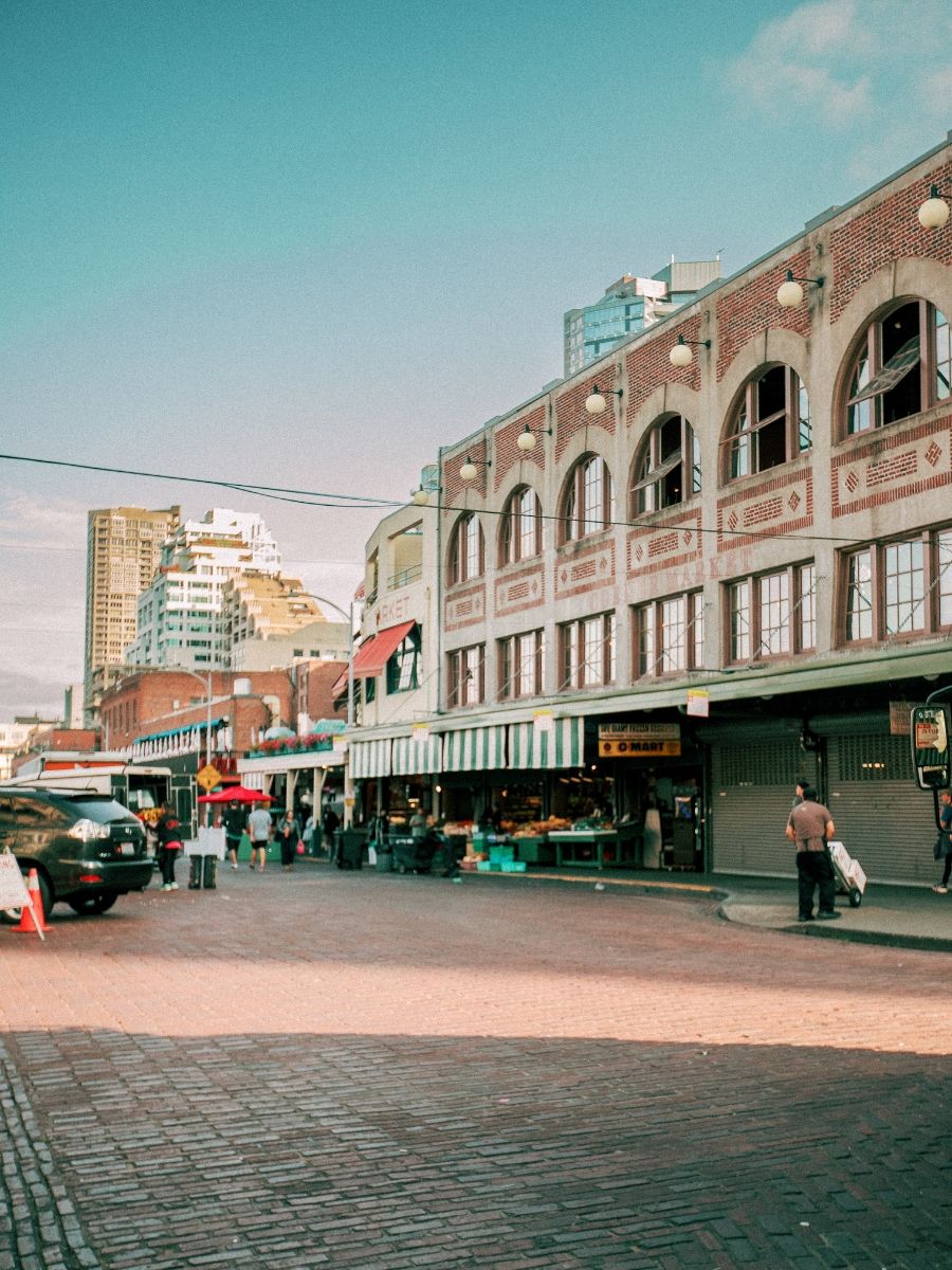 Pike Place Market in Seattle with brick buildings, street vendors, and pedestrians on a cobblestone plaza.