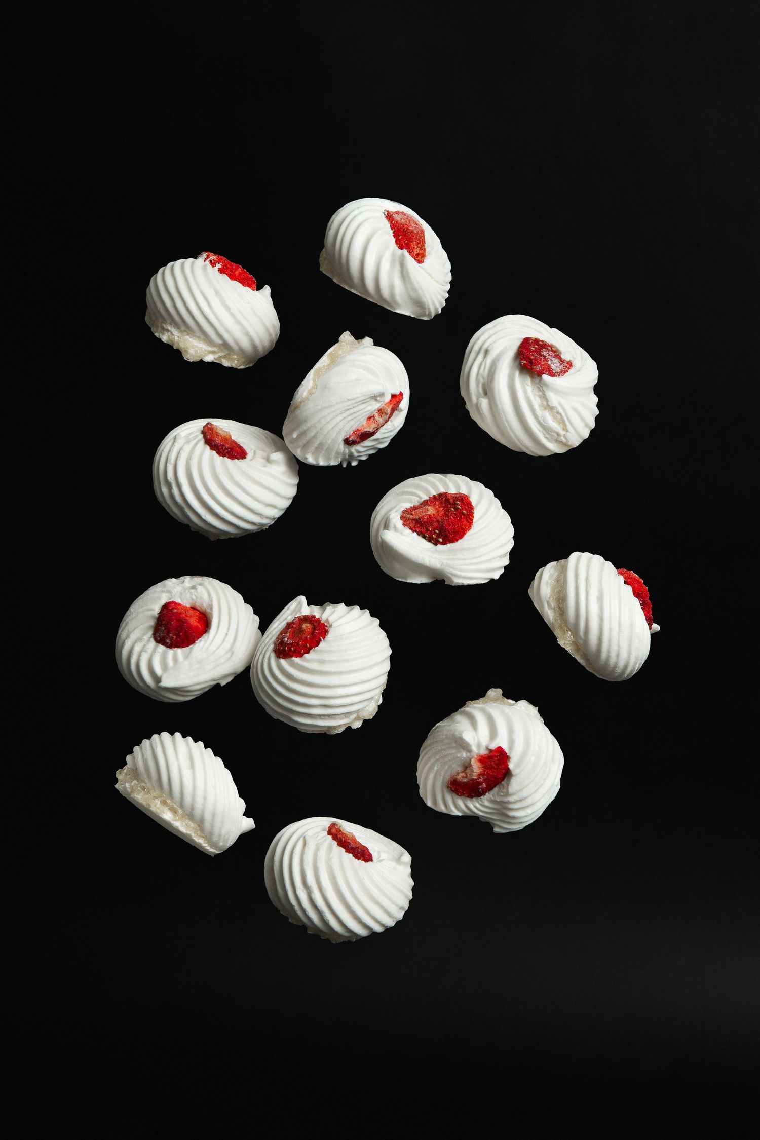 White meringue cookies topped with fresh strawberry pieces arranged on a dark black background.