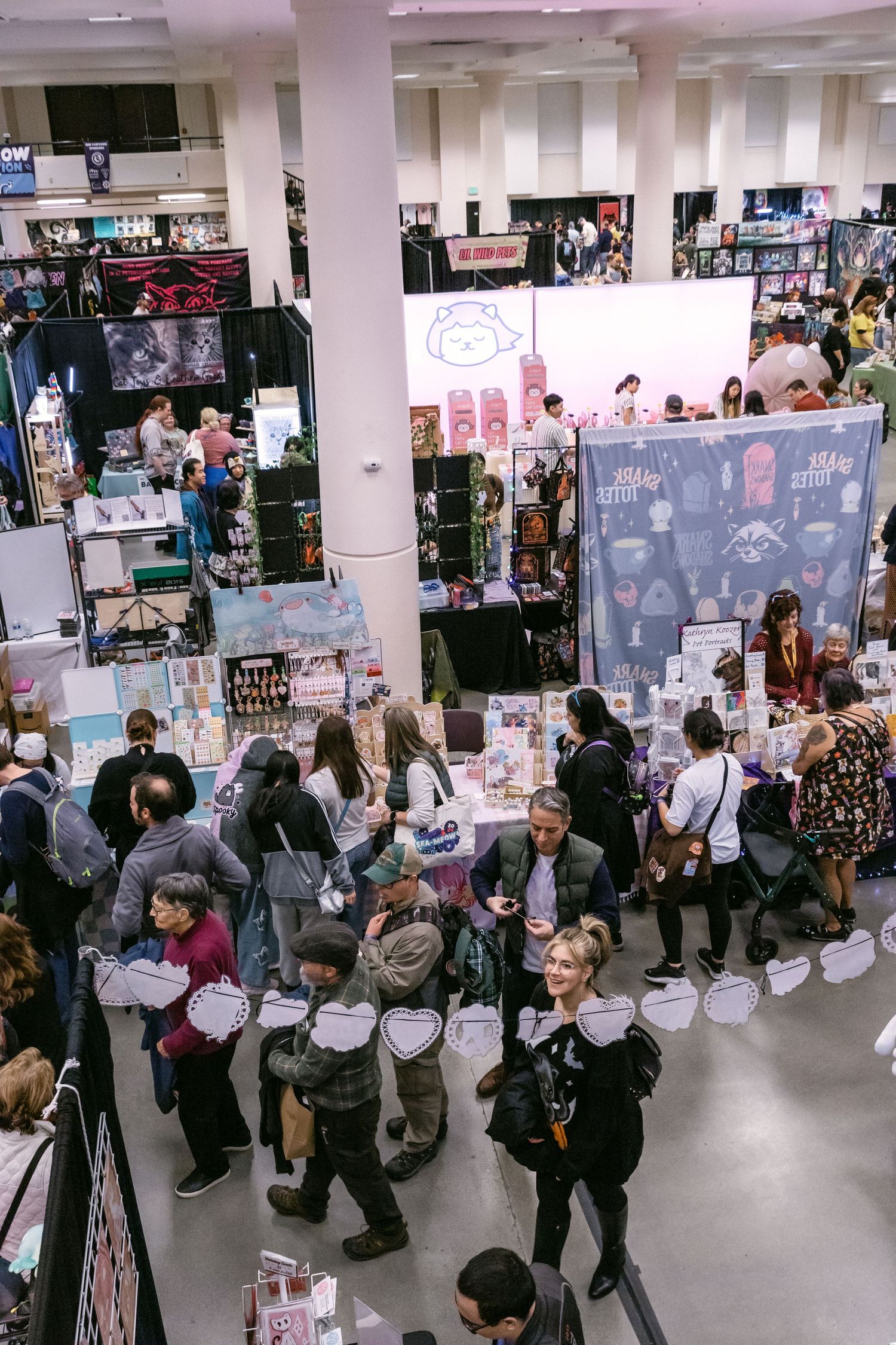 Overhead view of a busy indoor art and craft fair with vendors and shoppers browsing colorful booths.
