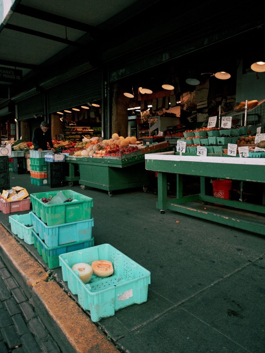 Outdoor farmers market with green display tables and crates filled with fresh fruits and vegetables at Pike Place Market.