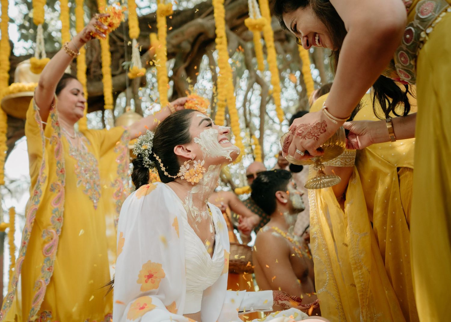 People wearing yellow celebrating a traditional Haldi ceremony with turmeric powder during Indian pre-wedding festivities.