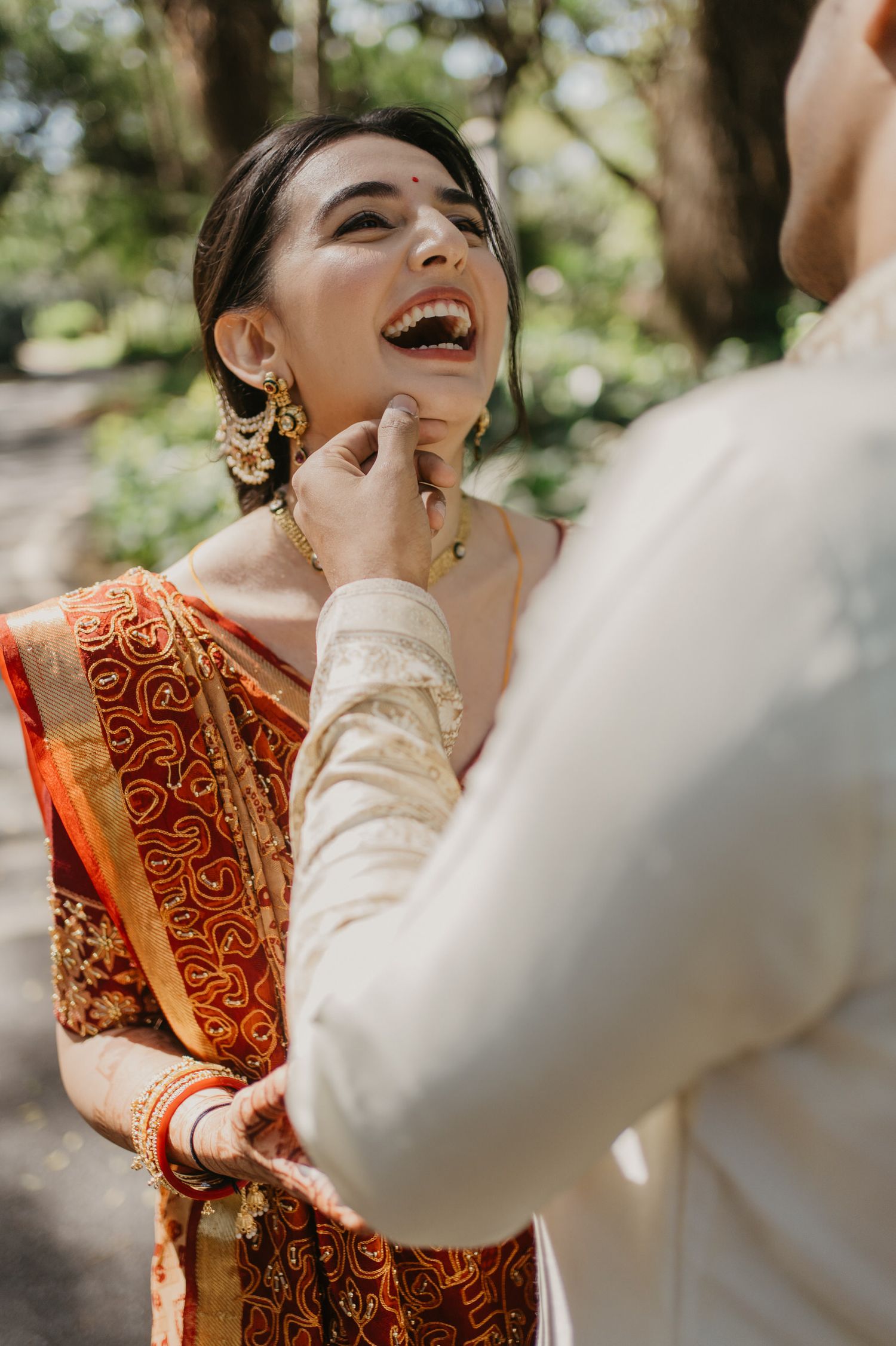 Beautiful candid moment in traditional red and gold wedding attire outdoors with ornate jewelry and joyful expression.