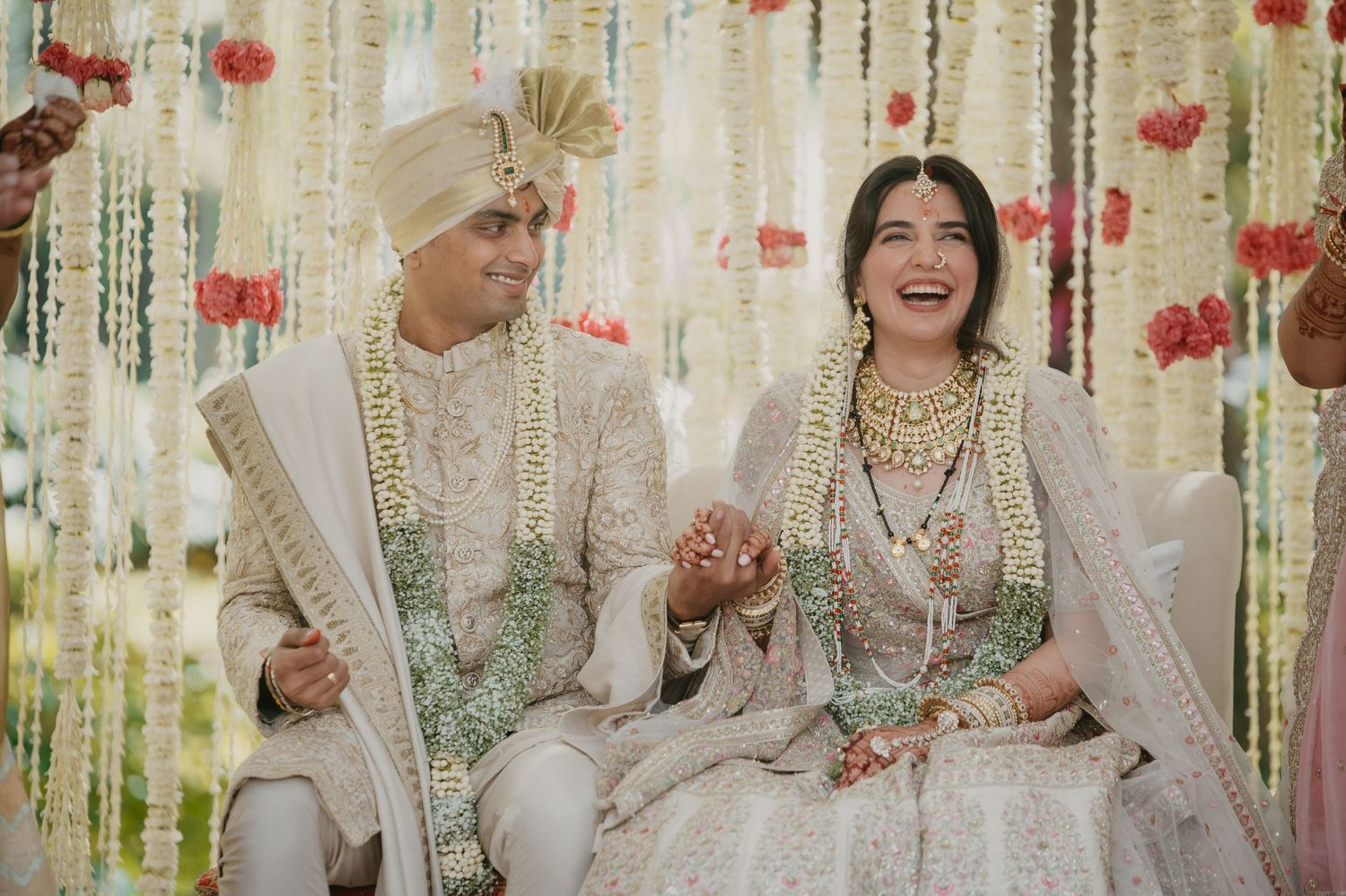 A couple shares a joyful moment at their wedding ceremony in traditional South Asian attire with floral decorations.