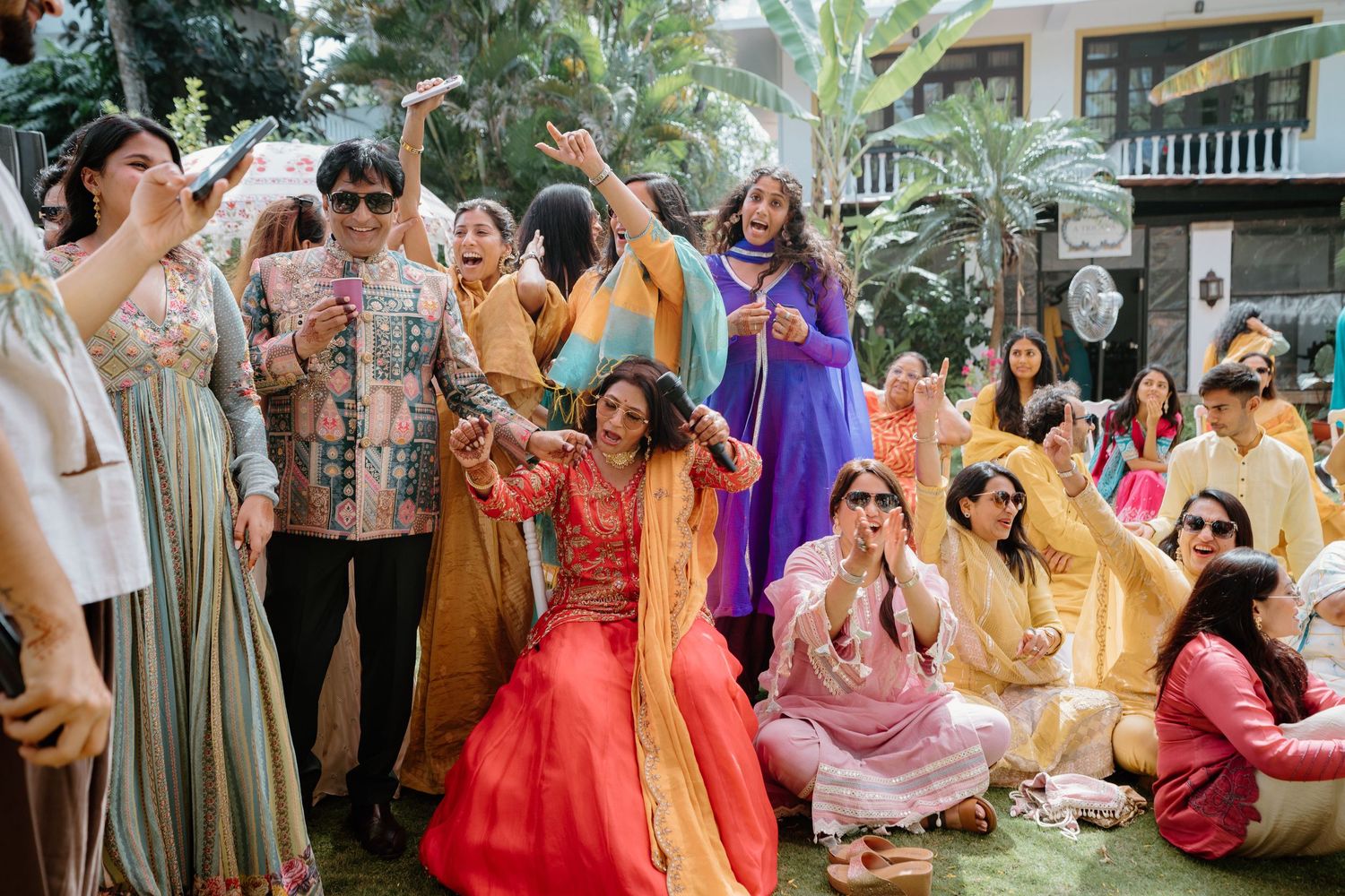 Joyful guests in colorful traditional Indian attire celebrate outdoors at a festive wedding ceremony.