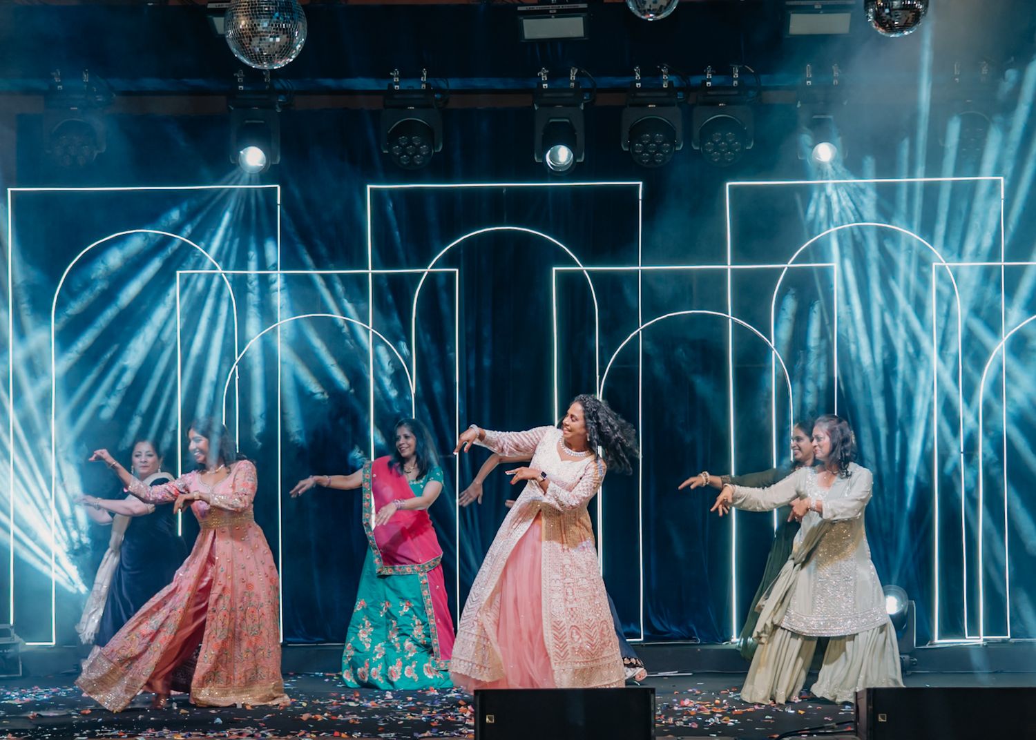 Dancers in flowing dresses perform a synchronized routine on stage with blue lighting effects.