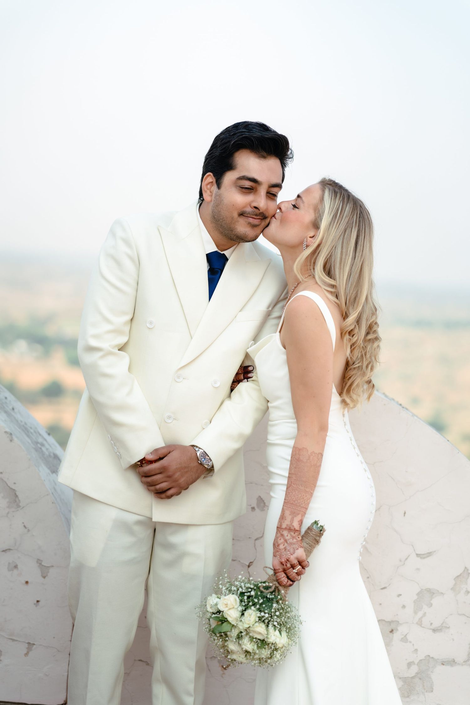 Intimate wedding portrait against desert landscape with couple in cream and white attire.