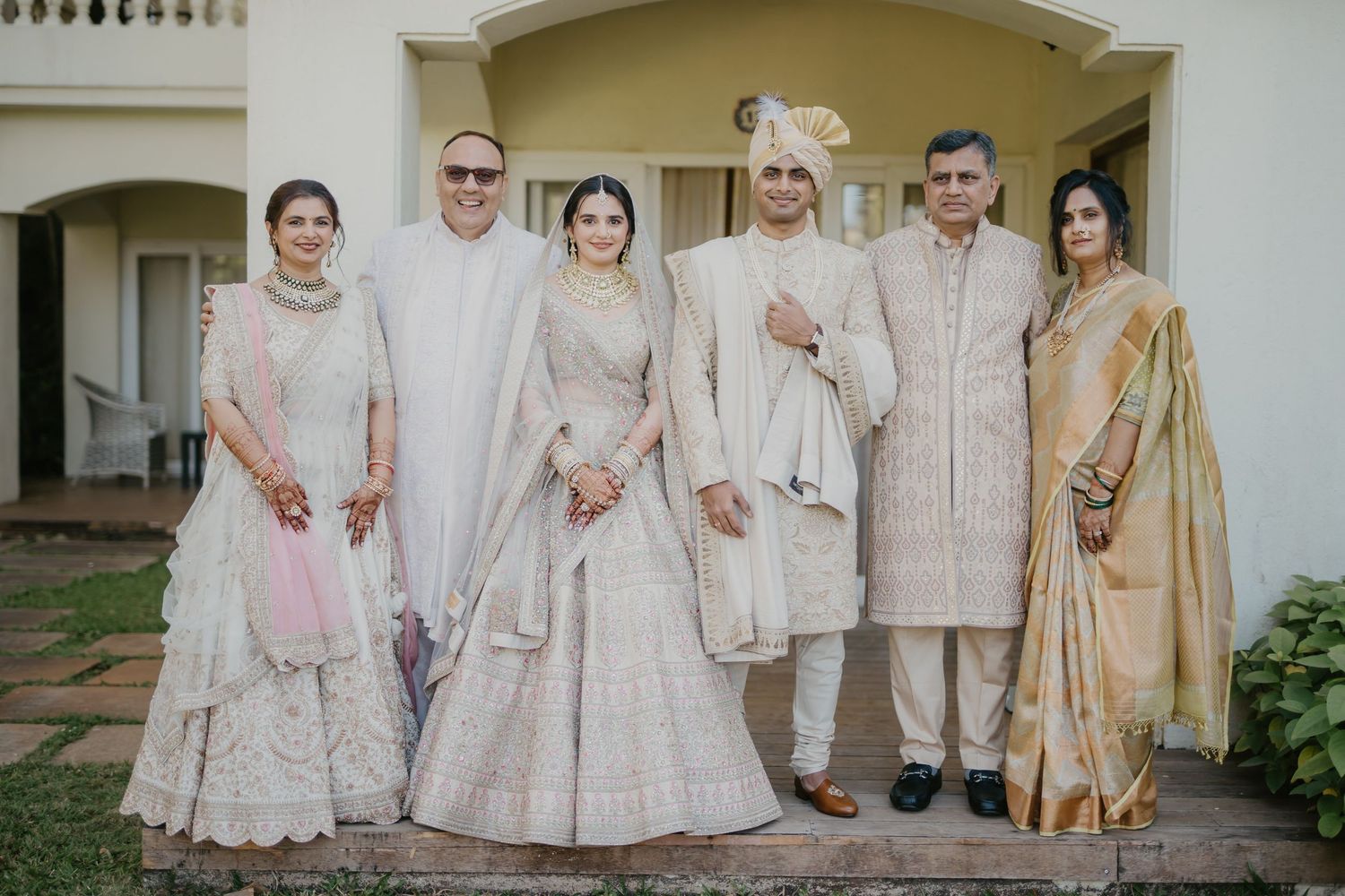 Traditional wedding party members wearing coordinated cream and beige outfits pose together outdoors.