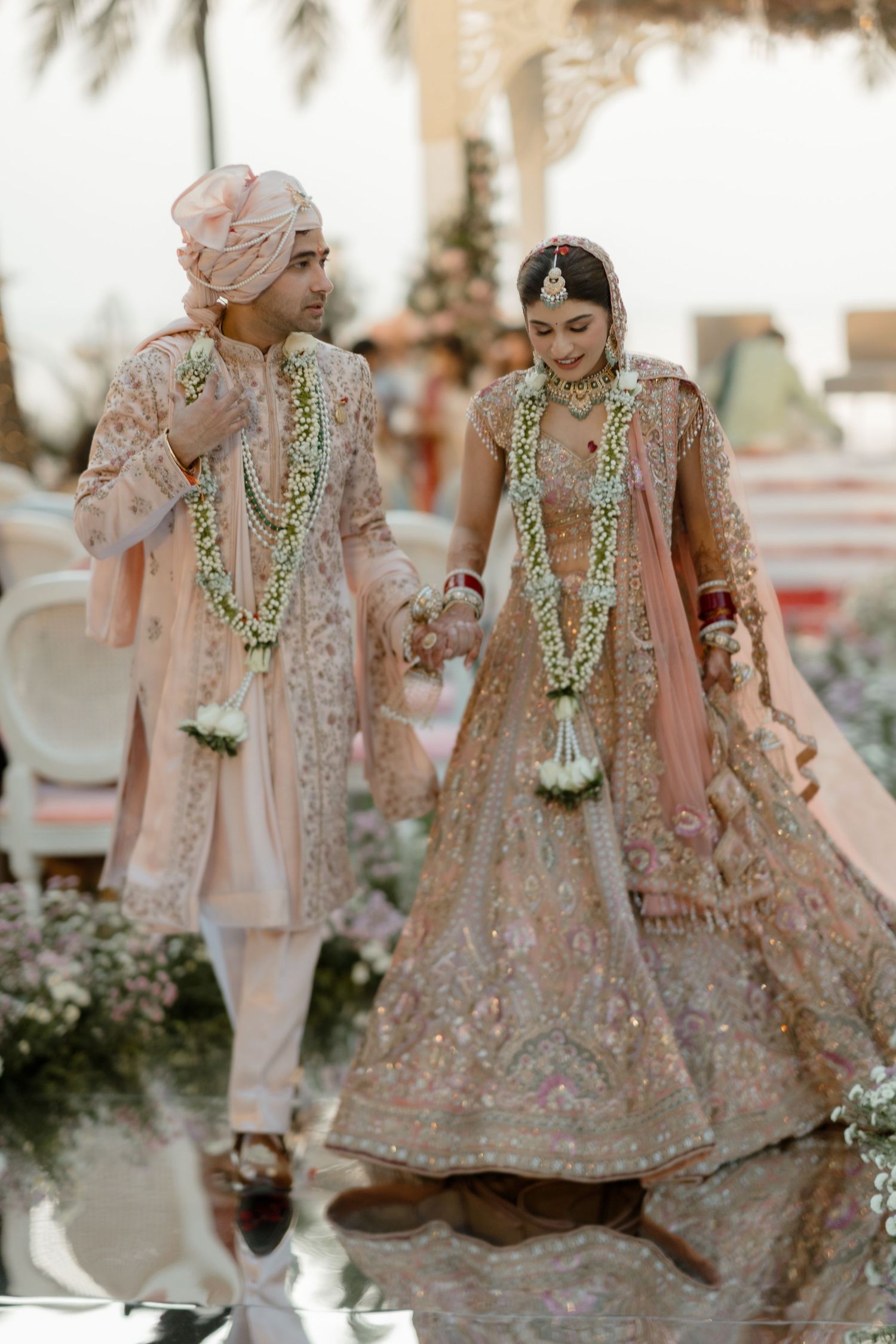 Traditional Indian wedding couple in pastel pink outfits adorned with floral garlands during their ceremony.