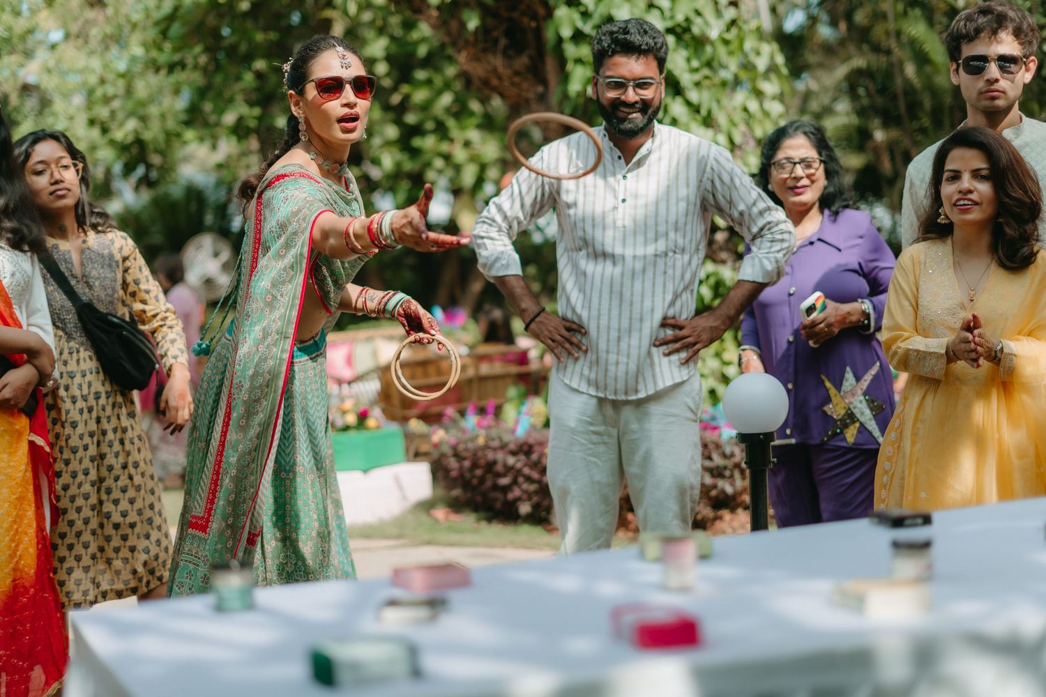 Joyful Indian couple playing badminton at an outdoor celebration, surrounded by guests in colorful traditional attire.