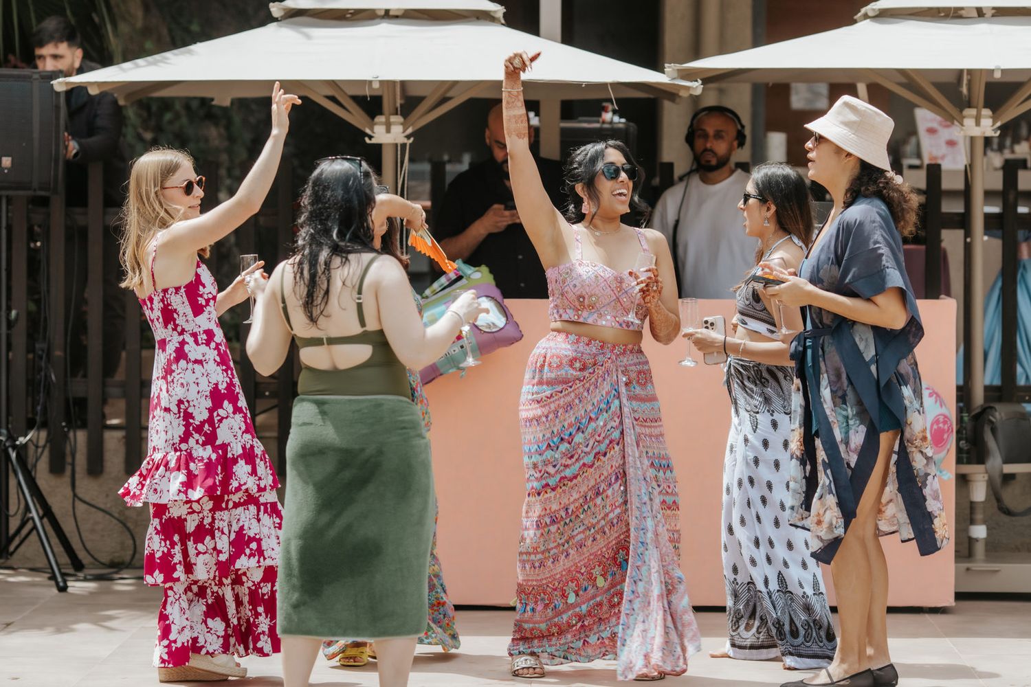 Group of women in colorful summer dresses dancing outdoors at a sunny social gathering.