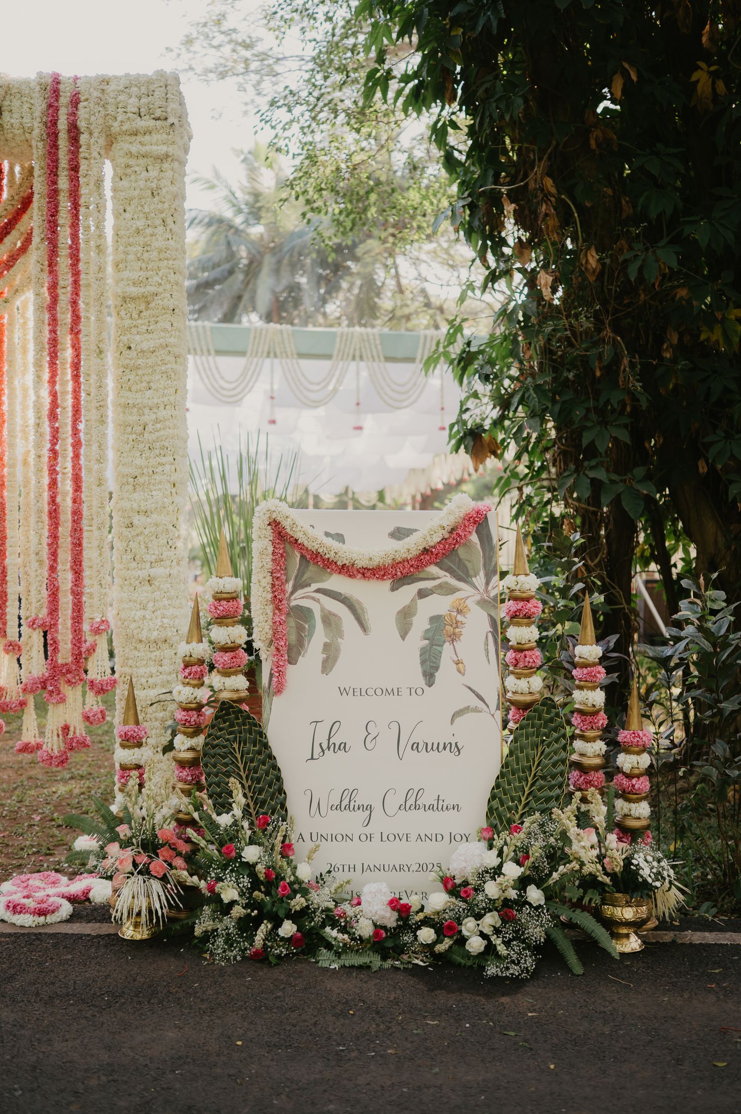 Elegant wedding welcome sign with pink floral decorations and hanging lanterns in a romantic outdoor garden setting.