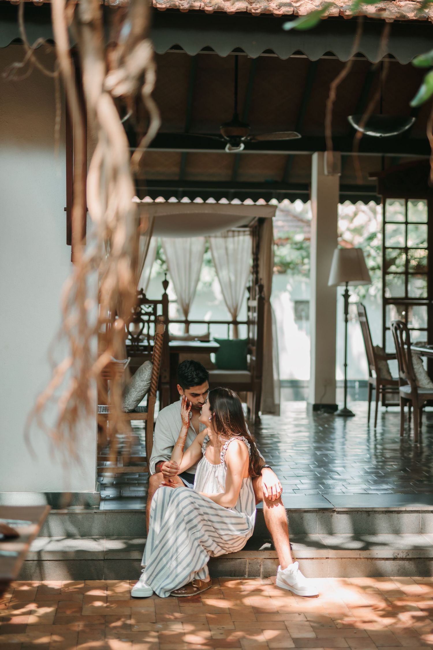 Sunlit interior scene with dappled shadows falling across a polished floor as someone relaxes in casual summer attire.