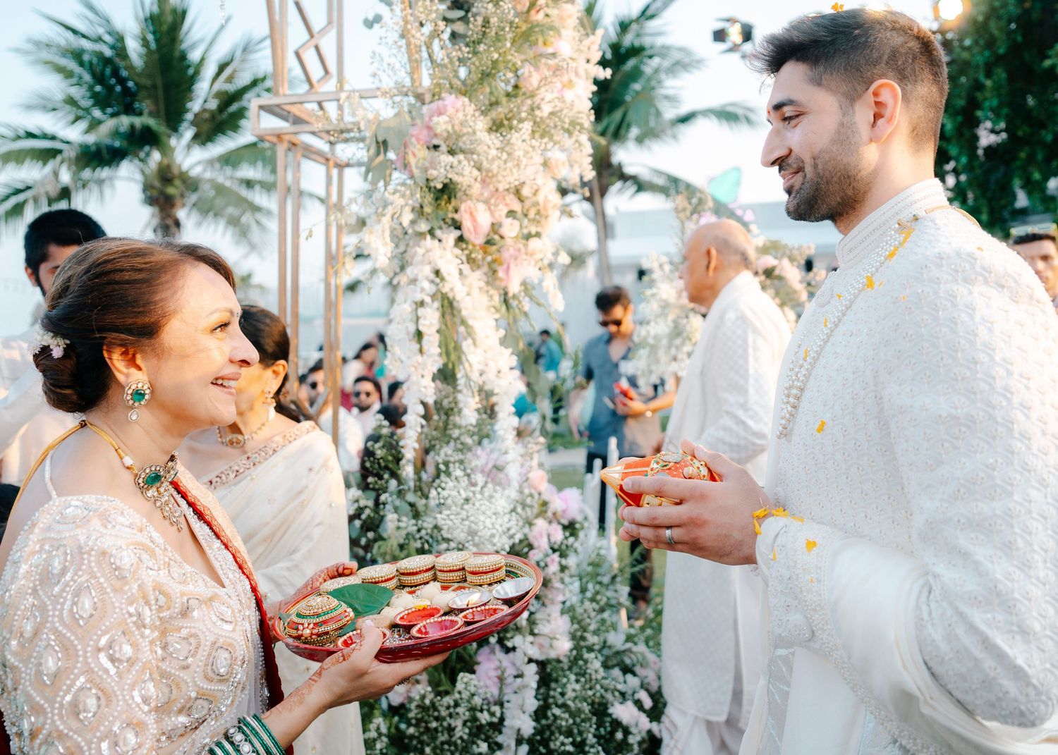 Wedding guests enjoying food and drinks at an elegant outdoor celebration decorated with palm trees and string lights.