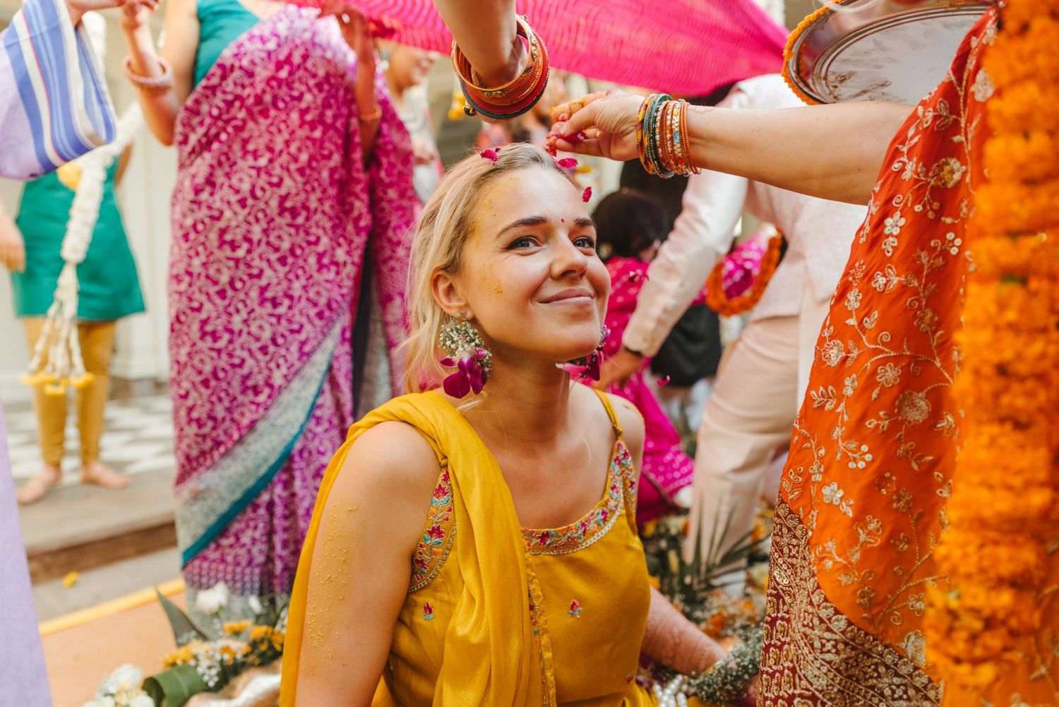 Joyful celebration with guests throwing pink flower petals against colorful decorative backdrop.