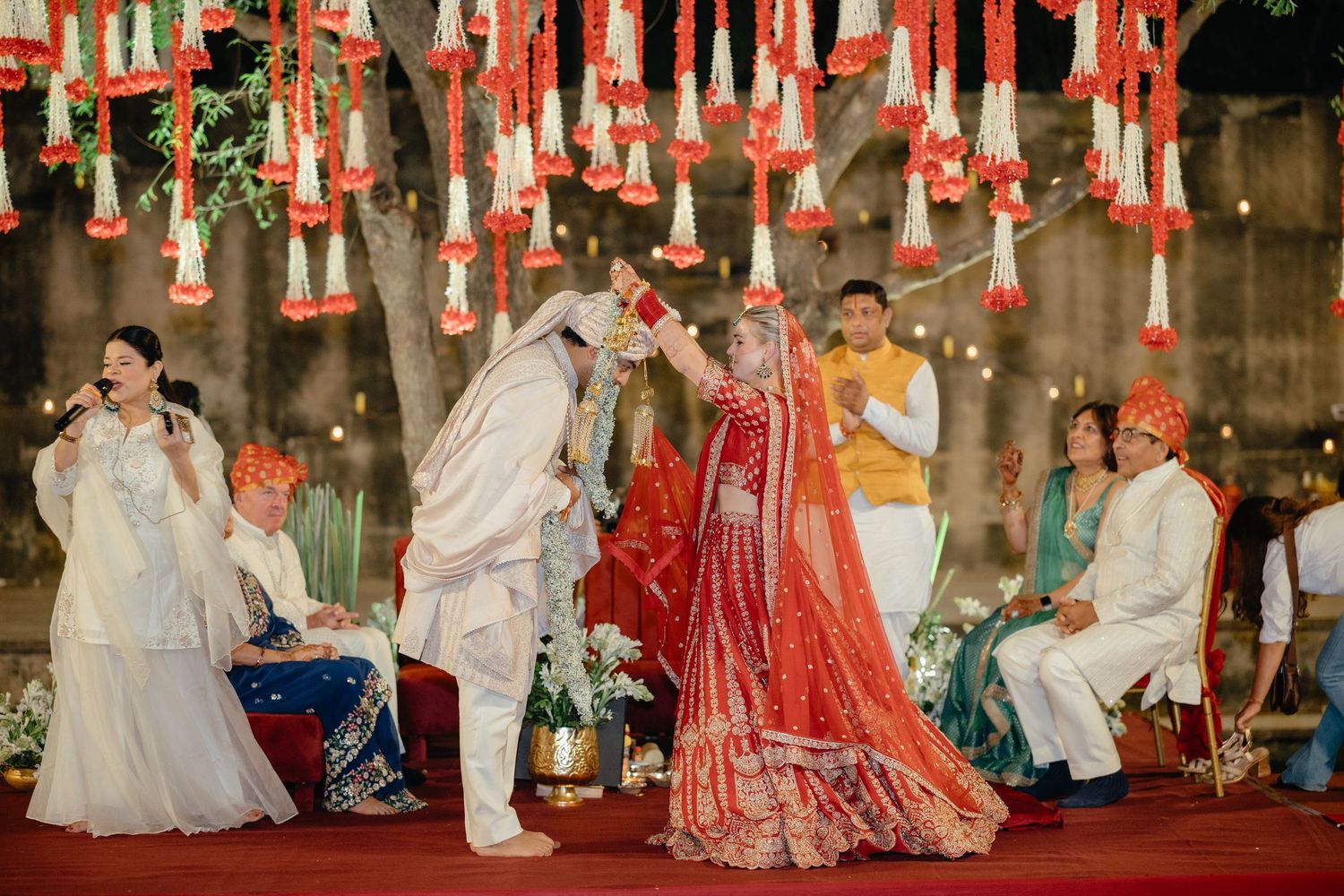 Outdoor wedding venue decorated with hanging red and white tassels and string lights.