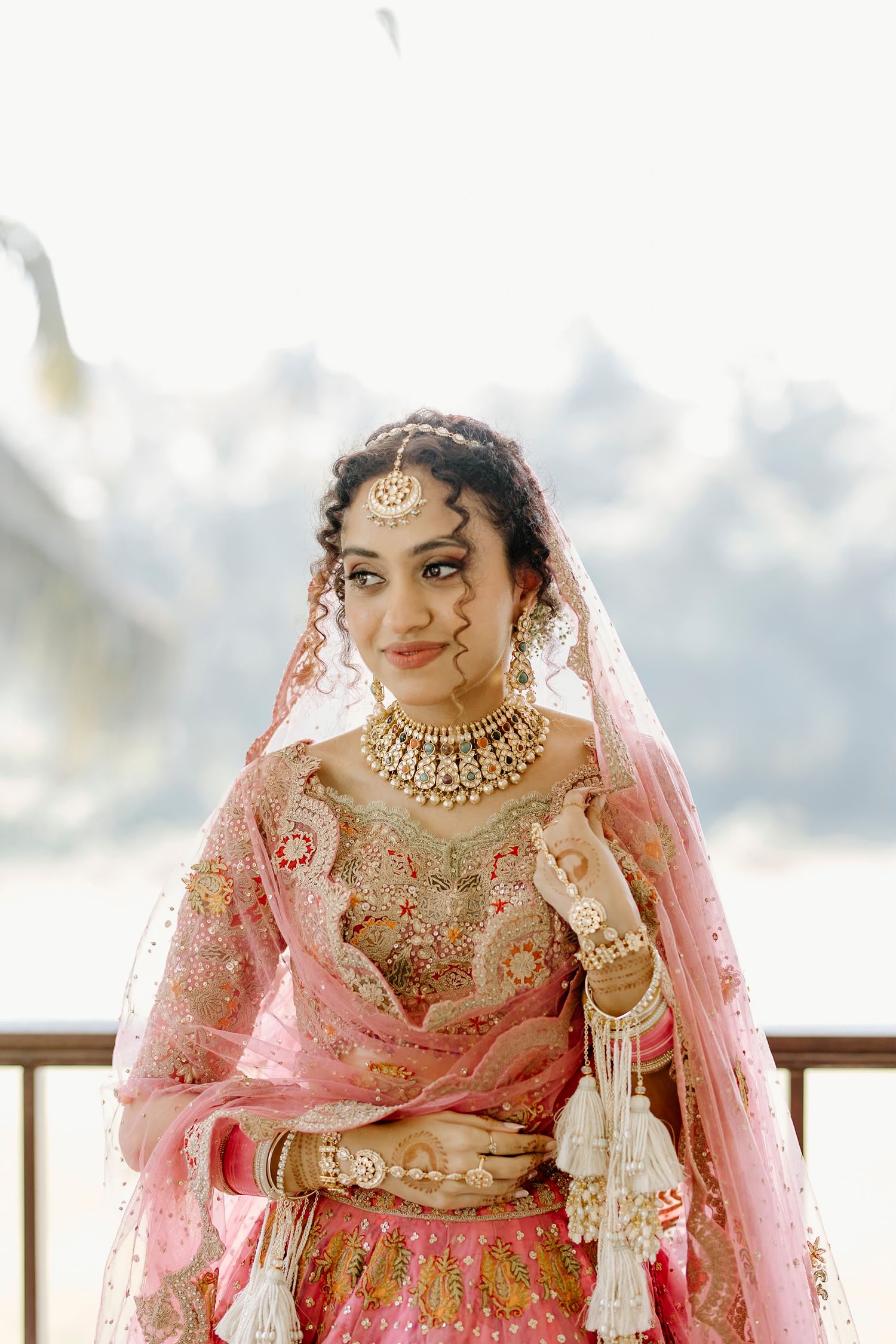 Traditional bridal attire with pink lehenga and ornate gold jewelry details.