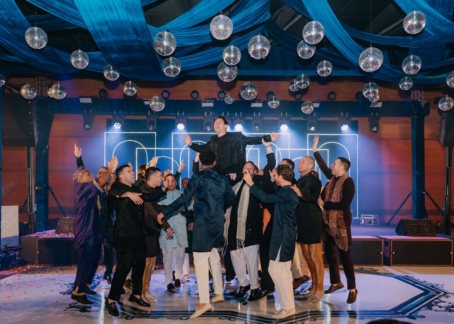 Large venue with disco balls hanging from ceiling and guests mingling on dance floor.