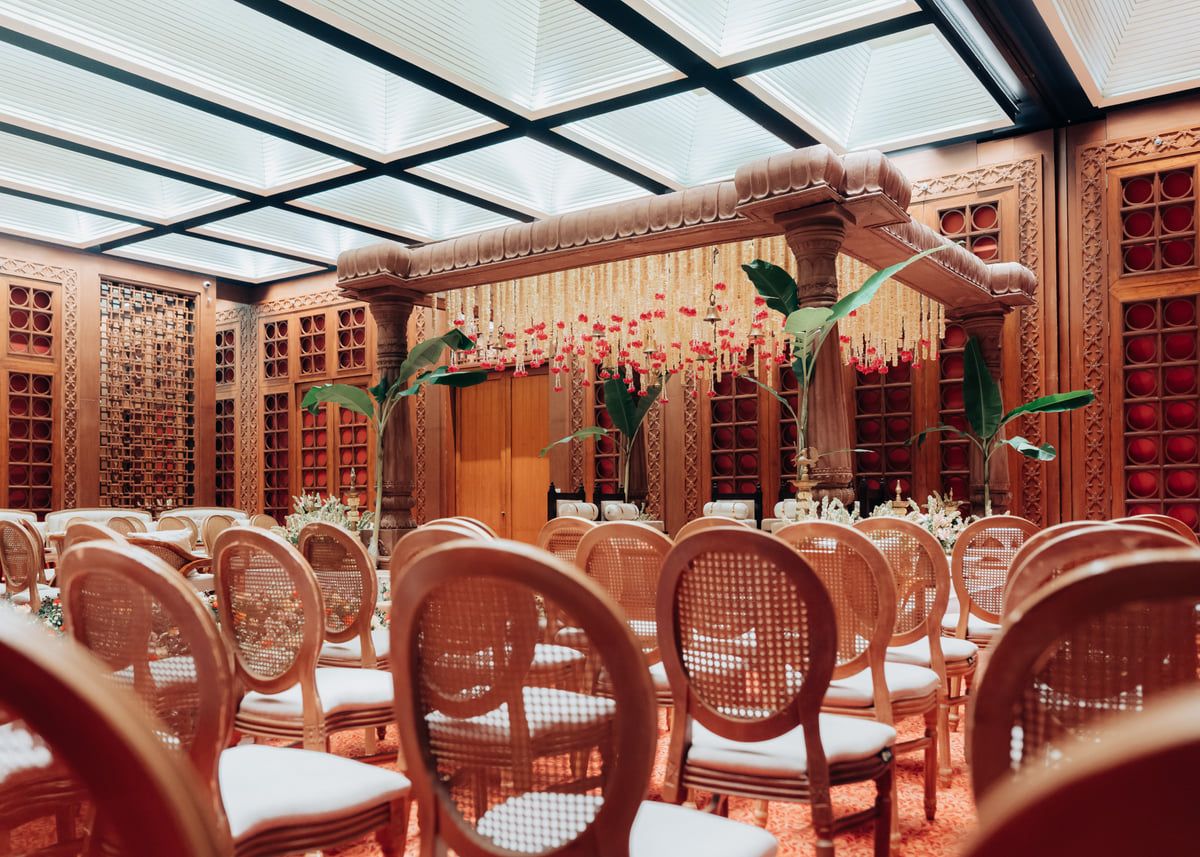 Elegant banquet hall with wooden paneling and cane-back chairs arranged in rows under a glass ceiling.