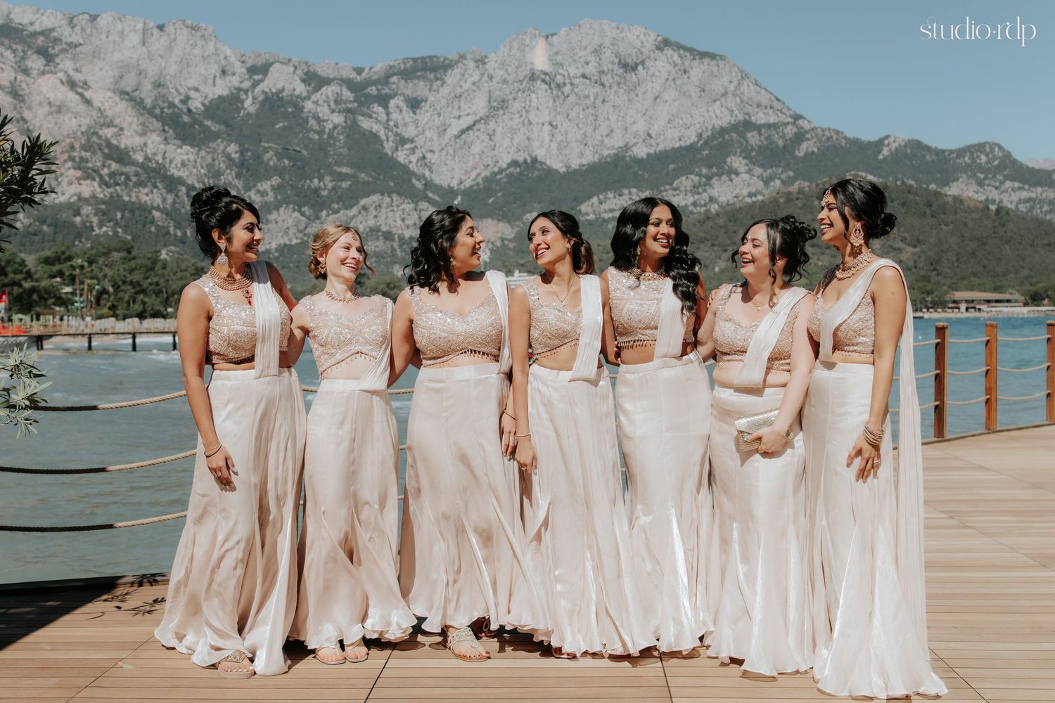 Seven bridesmaids in matching champagne gowns pose on a dock with stunning mountain backdrop.