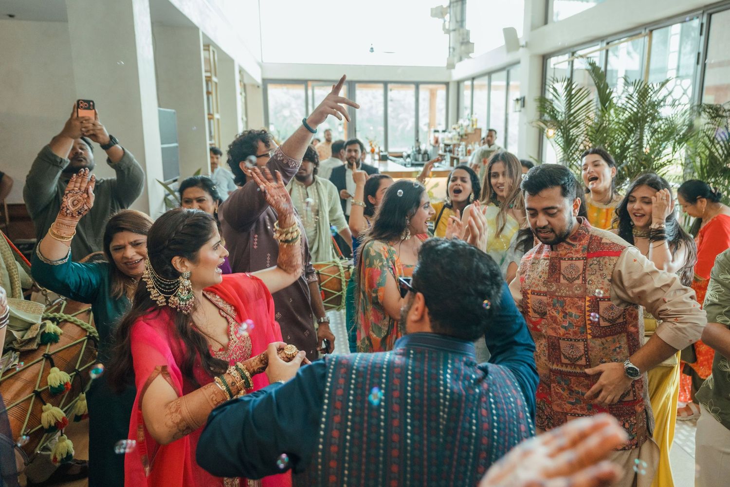 Vibrant Indian wedding celebration with guests dancing and cheering in colorful traditional attire at a festive indoor ceremony.