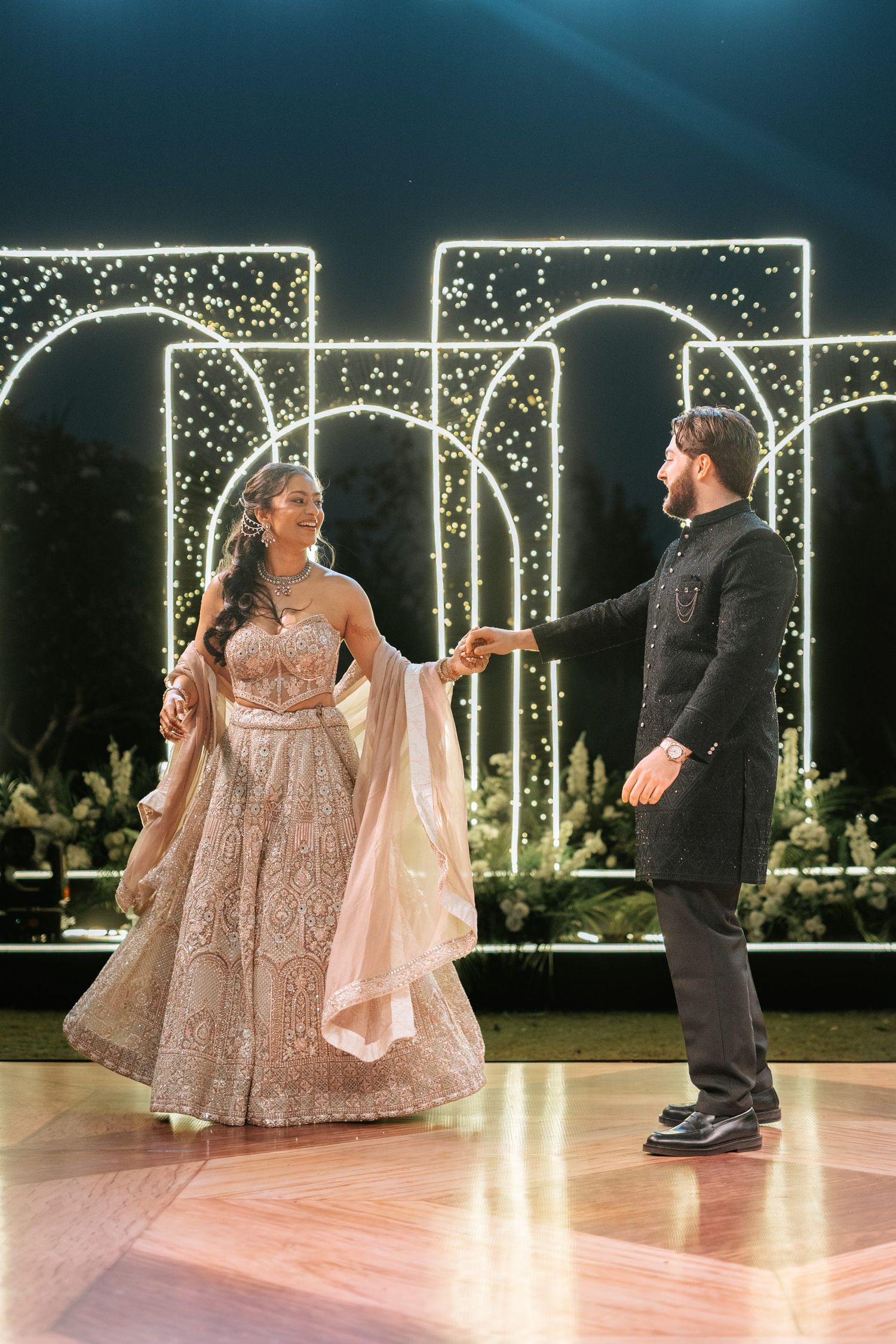 Couple sharing a romantic dance at an Indian wedding reception with elegant fairy light arch backdrop.