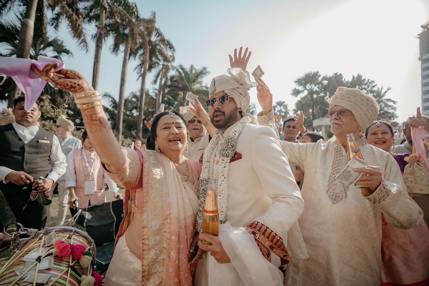 Joyful wedding guests wave their hands in celebration during golden hour at an outdoor tropical reception.