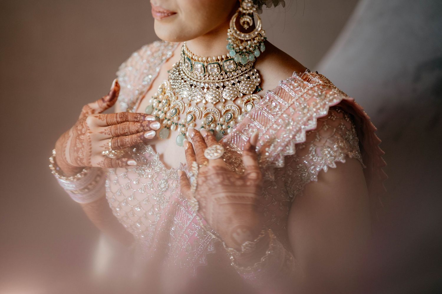 Close up detail of ornate bridal wear featuring pink lace sleeves and elaborate gold and crystal necklace jewelry.
