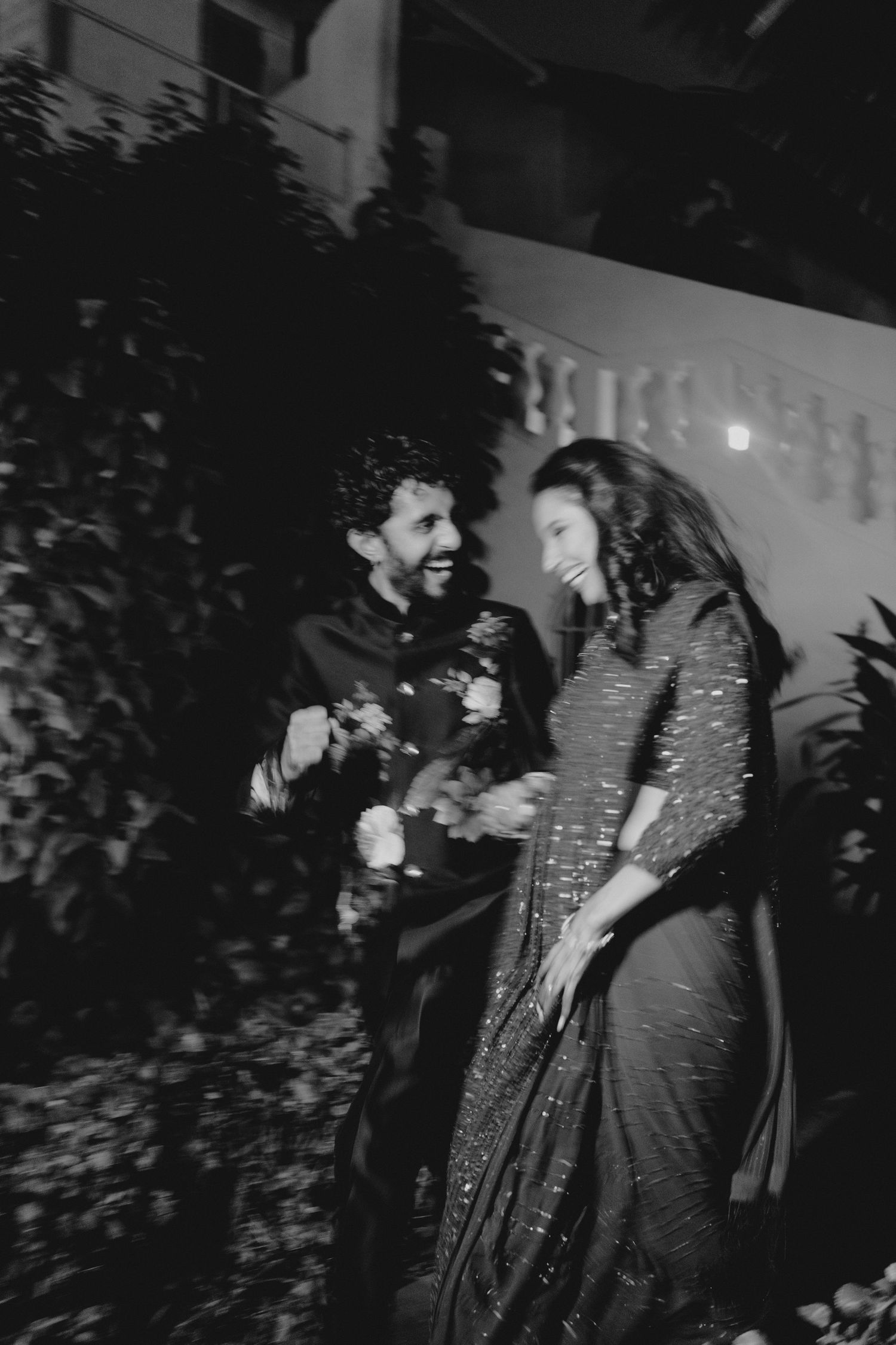 Black and white photo of a couple in traditional Indian attire laughing together outdoors at night.