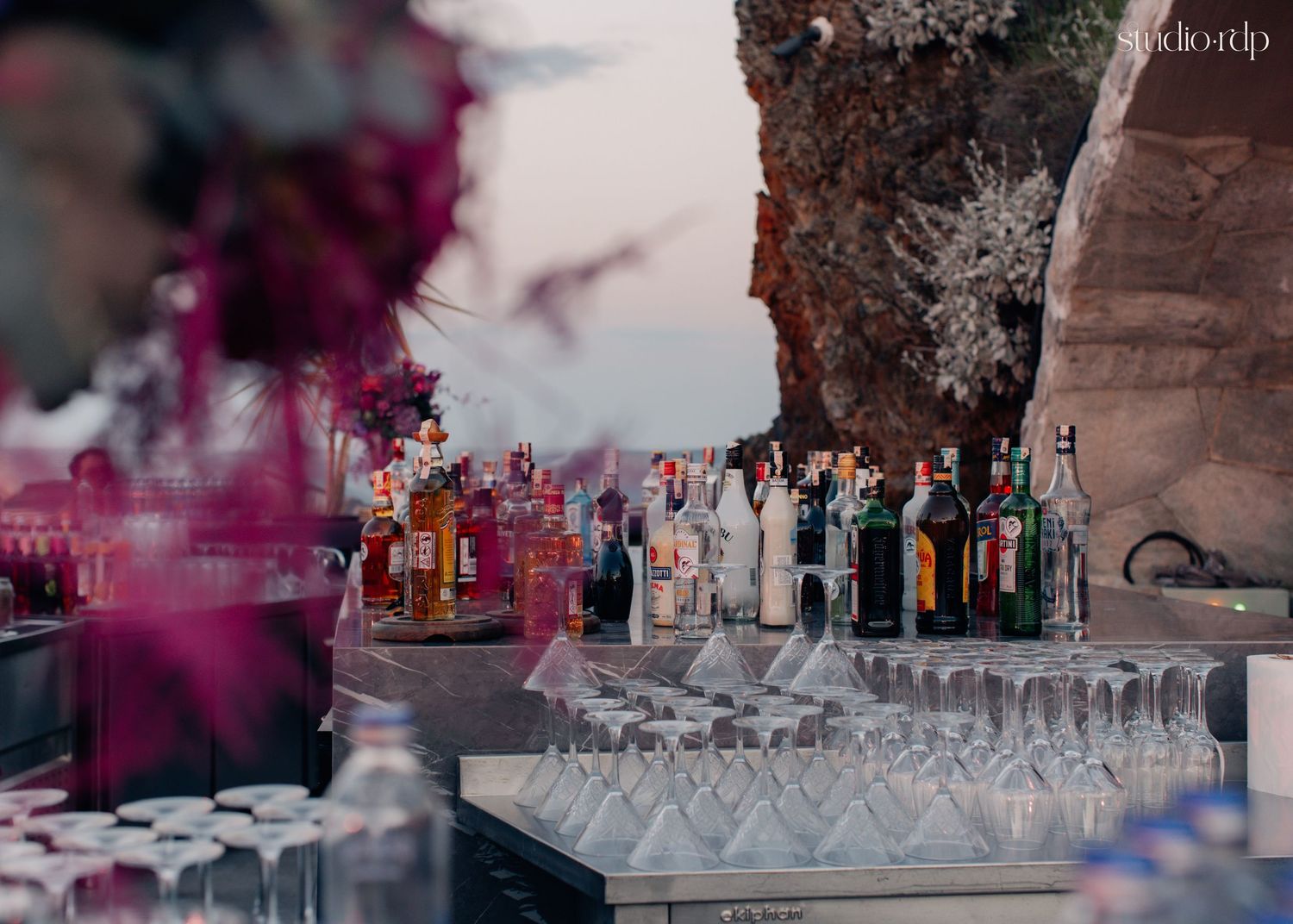 Elegant outdoor bar setup with colorful bottles and crystal glasses at a Santorini event venue.