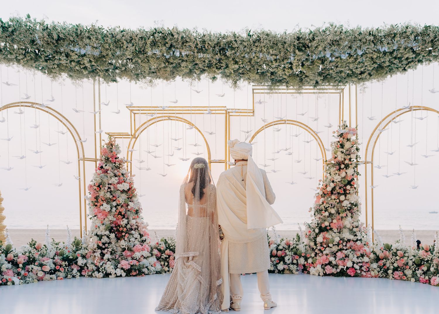 An elegant wedding ceremony space with floral arches and white decor against a light backdrop.