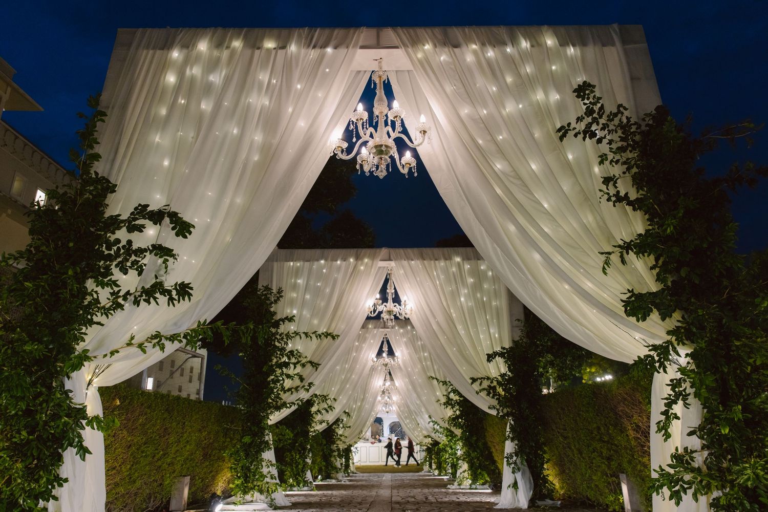 Outdoor wedding venue with white fabric draping and twinkling lights creating a magical atmosphere.