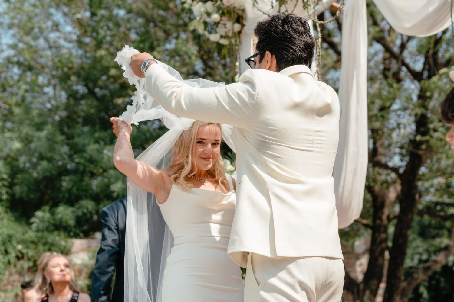 Couple dancing at outdoor wedding reception surrounded by white drapes and greenery.