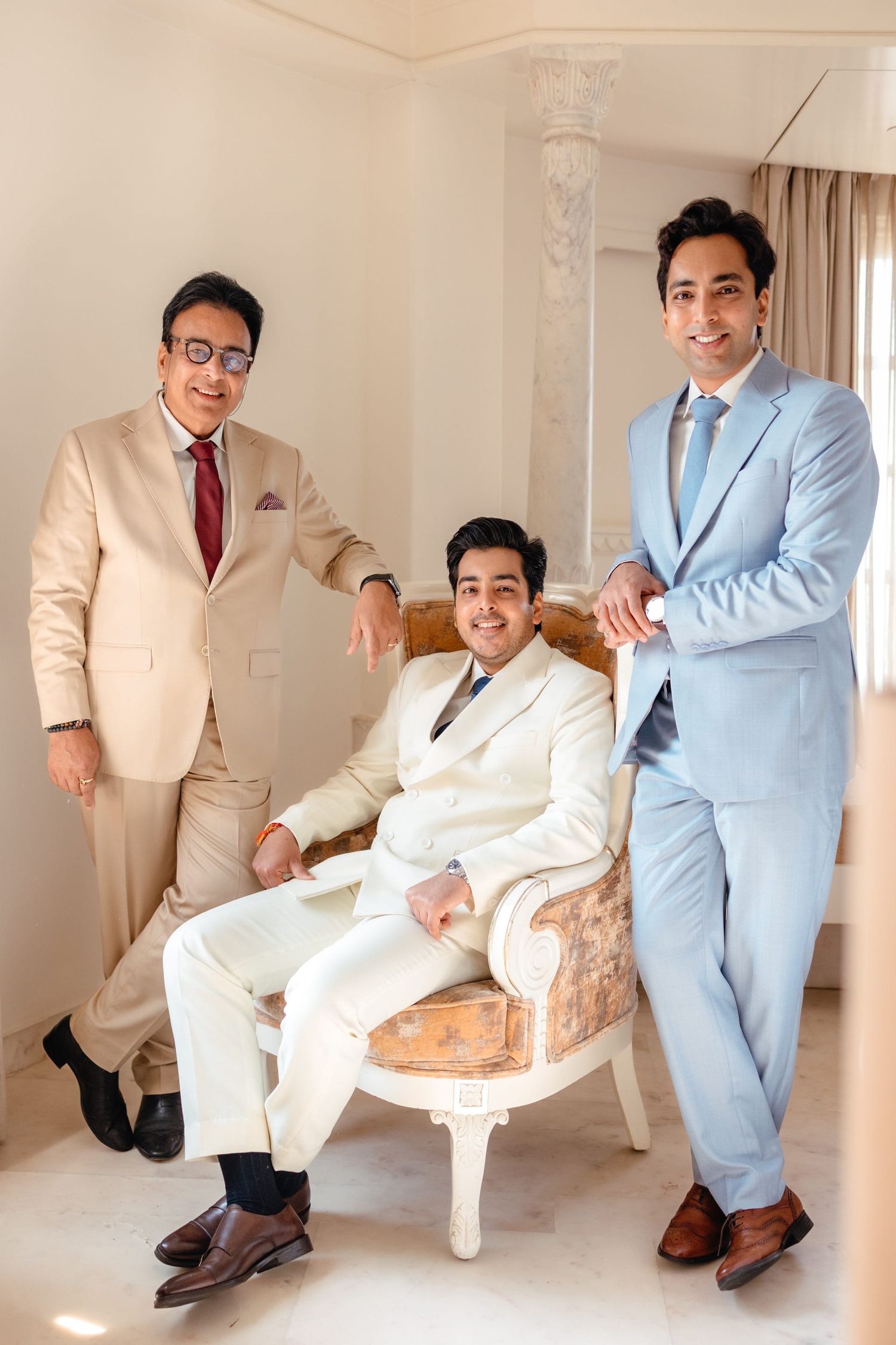 Groomsmen in light colored suits posing playfully on elegant white furniture.