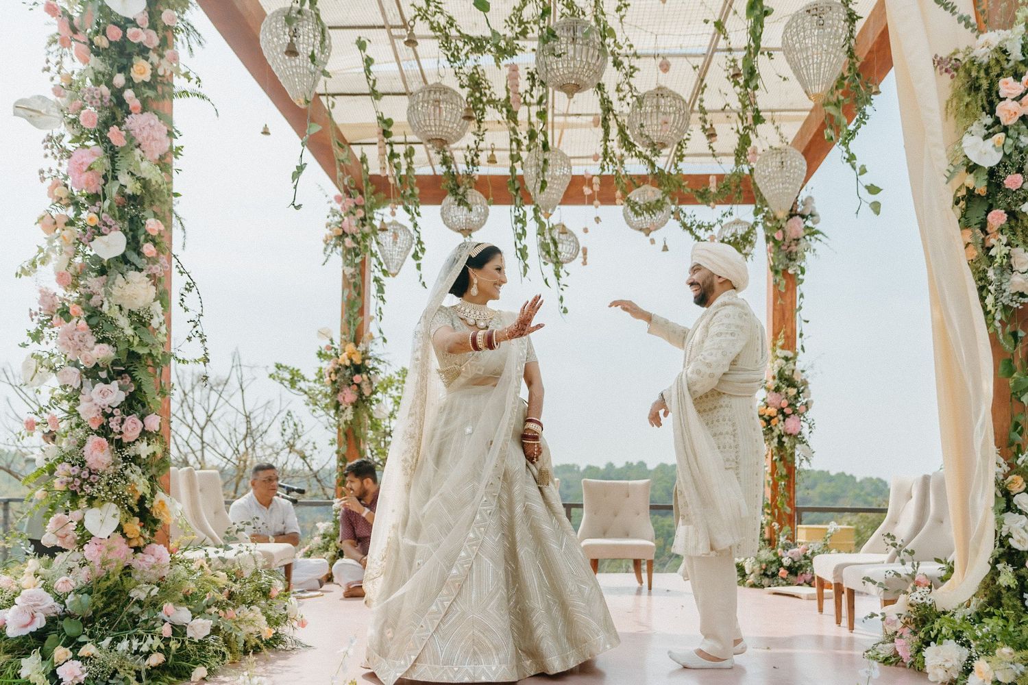Bride walking down a romantic beach wedding ceremony aisle decorated with flowing white curtains and tropical florals.