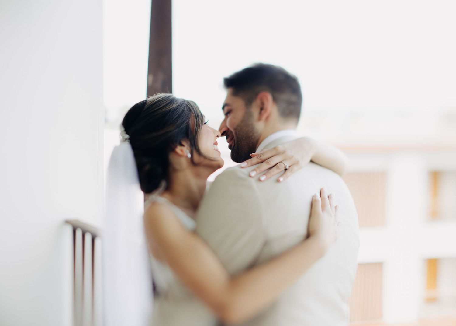A tender romantic moment between two people embracing in soft natural light on a balcony.