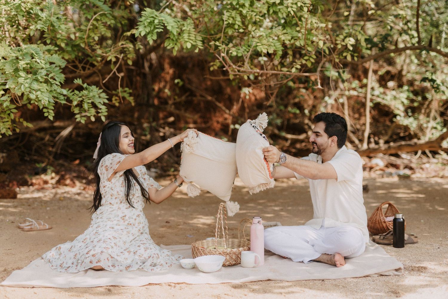 Friends enjoy a relaxing summer picnic on white blankets under shady trees in a park.