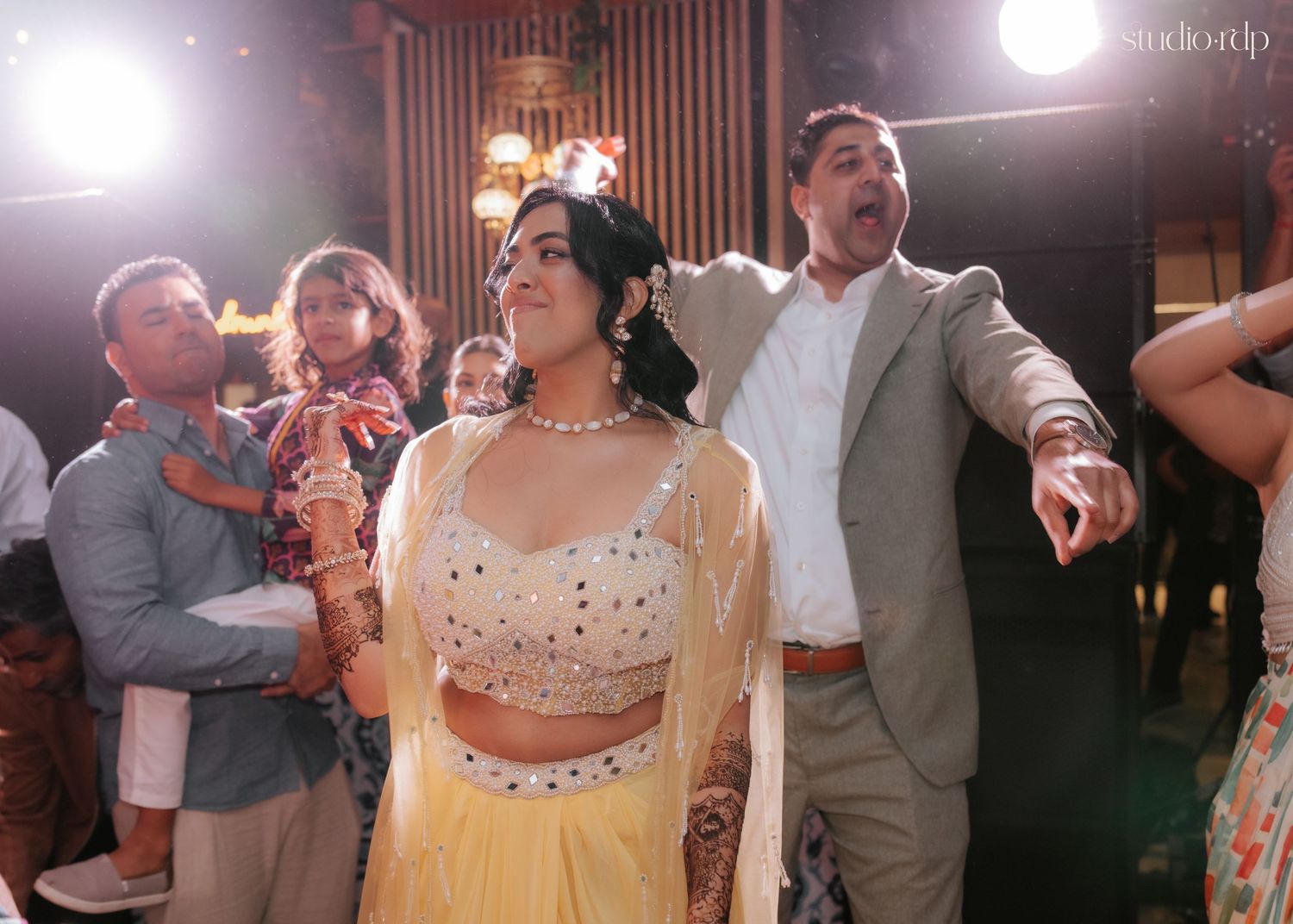 Bride in yellow lehenga dancing with guests at an Indian wedding celebration.