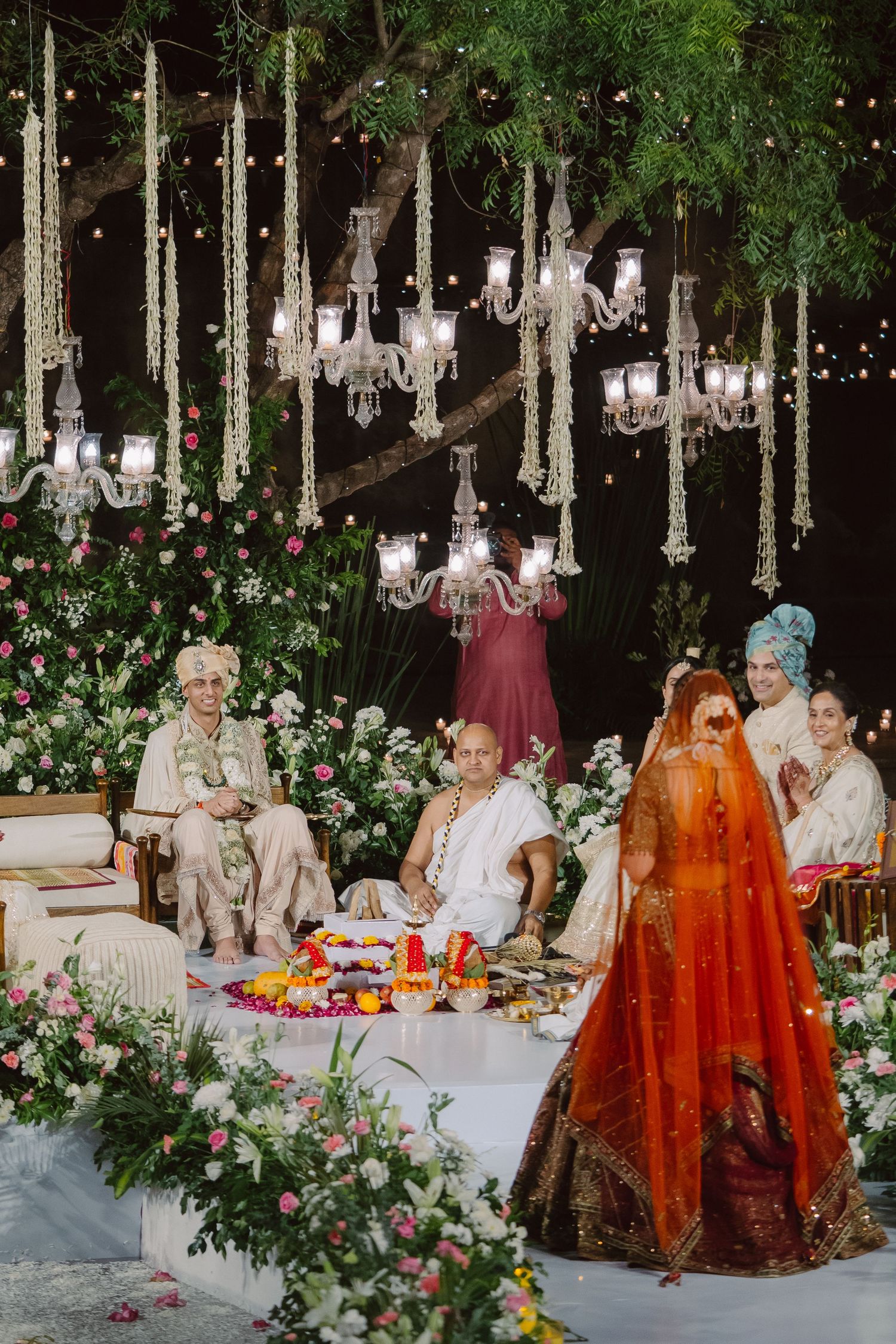 Romantic outdoor wedding venue with hanging chandeliers and floral arrangements.