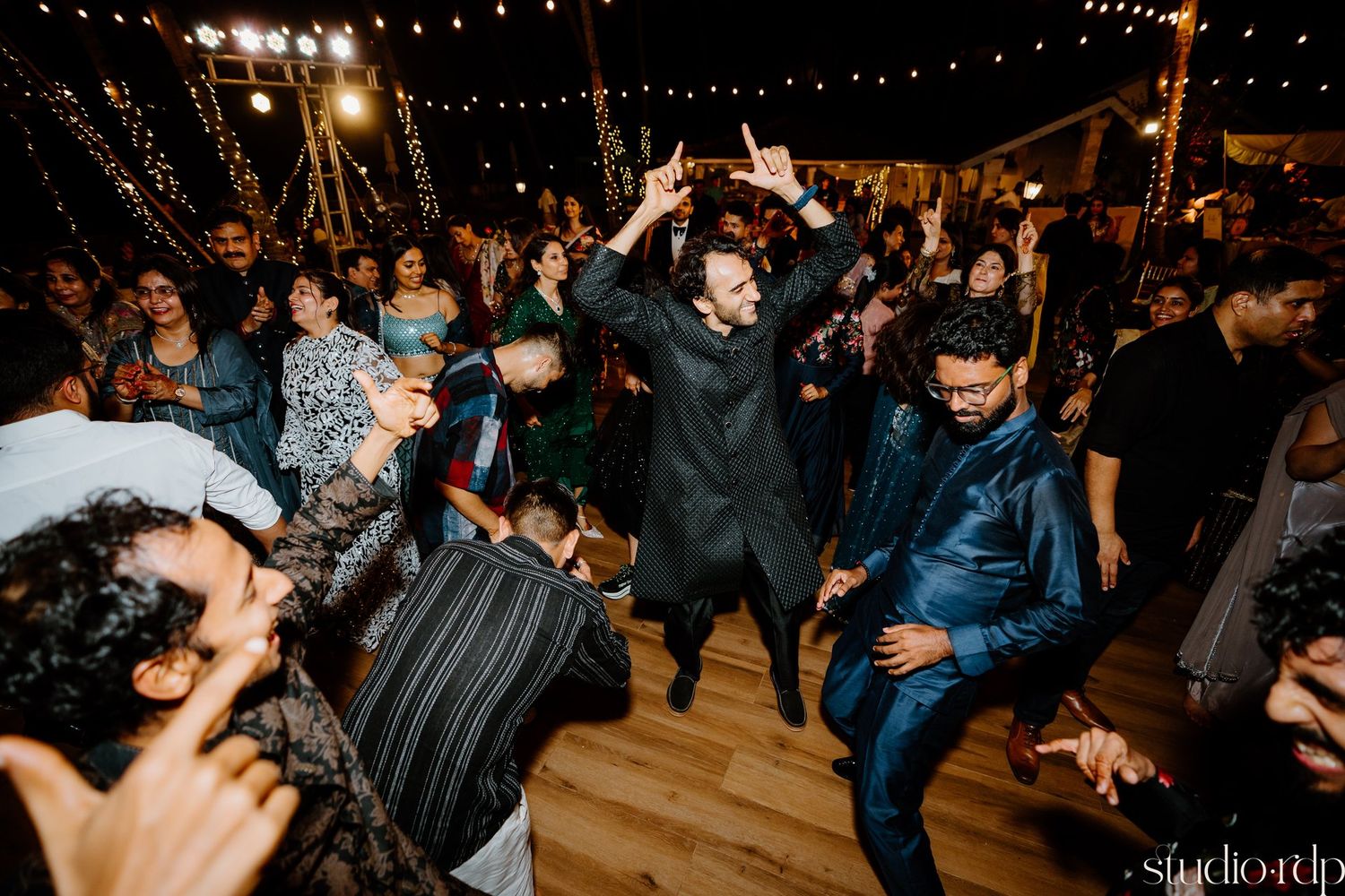 Guests dance enthusiastically on a wooden floor during a lively evening celebration.